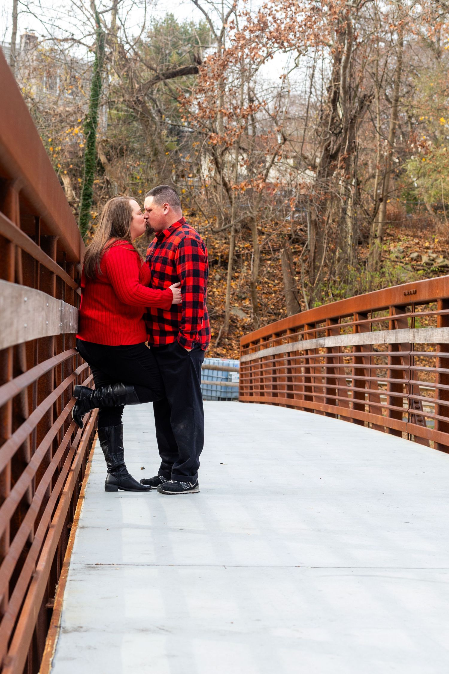 Couple in winter attire shares romantic moment on snow-covered wooden bridge.
