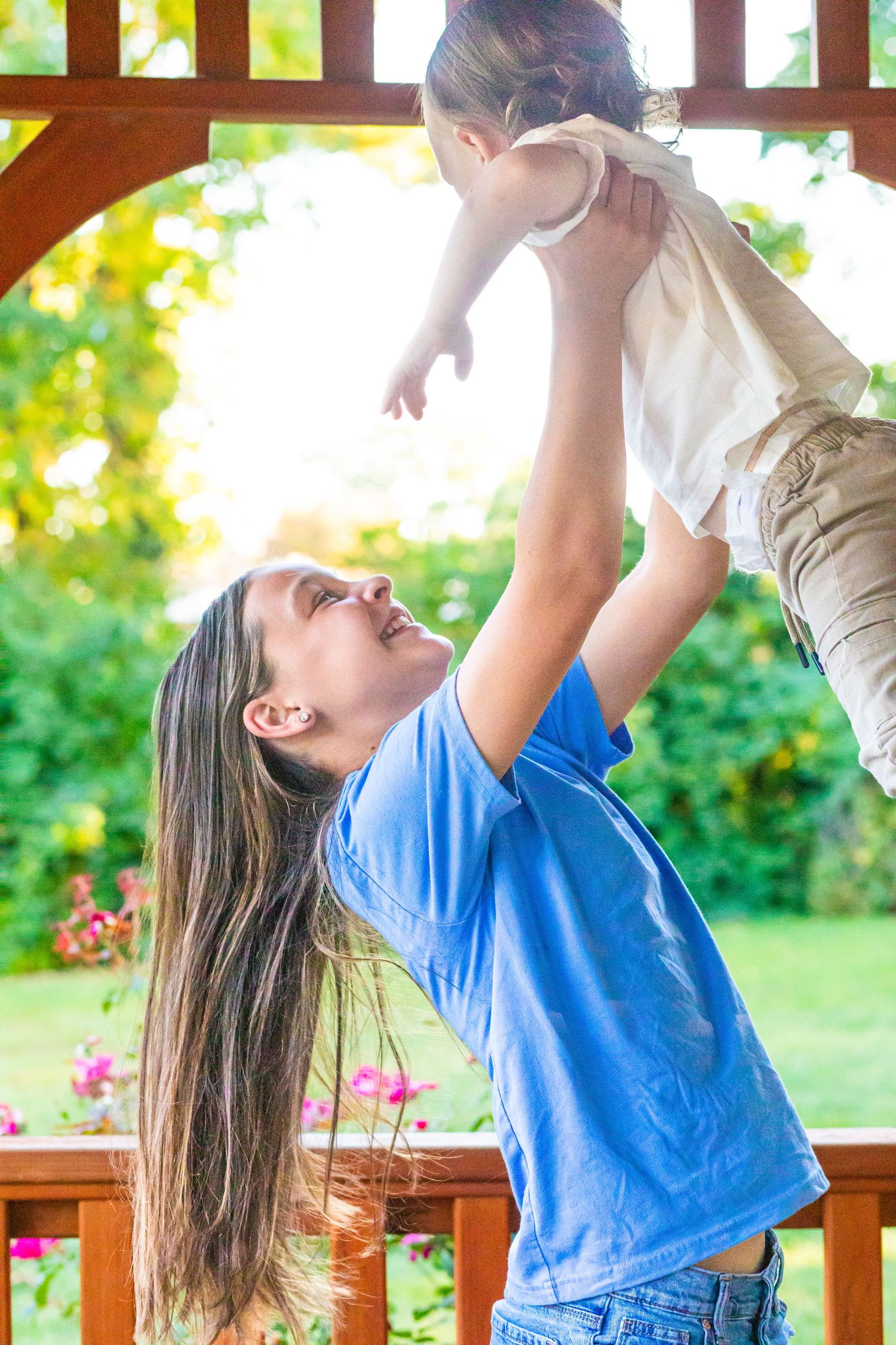 Person in blue shirt lifting and playing with children on outdoor wooden deck.
