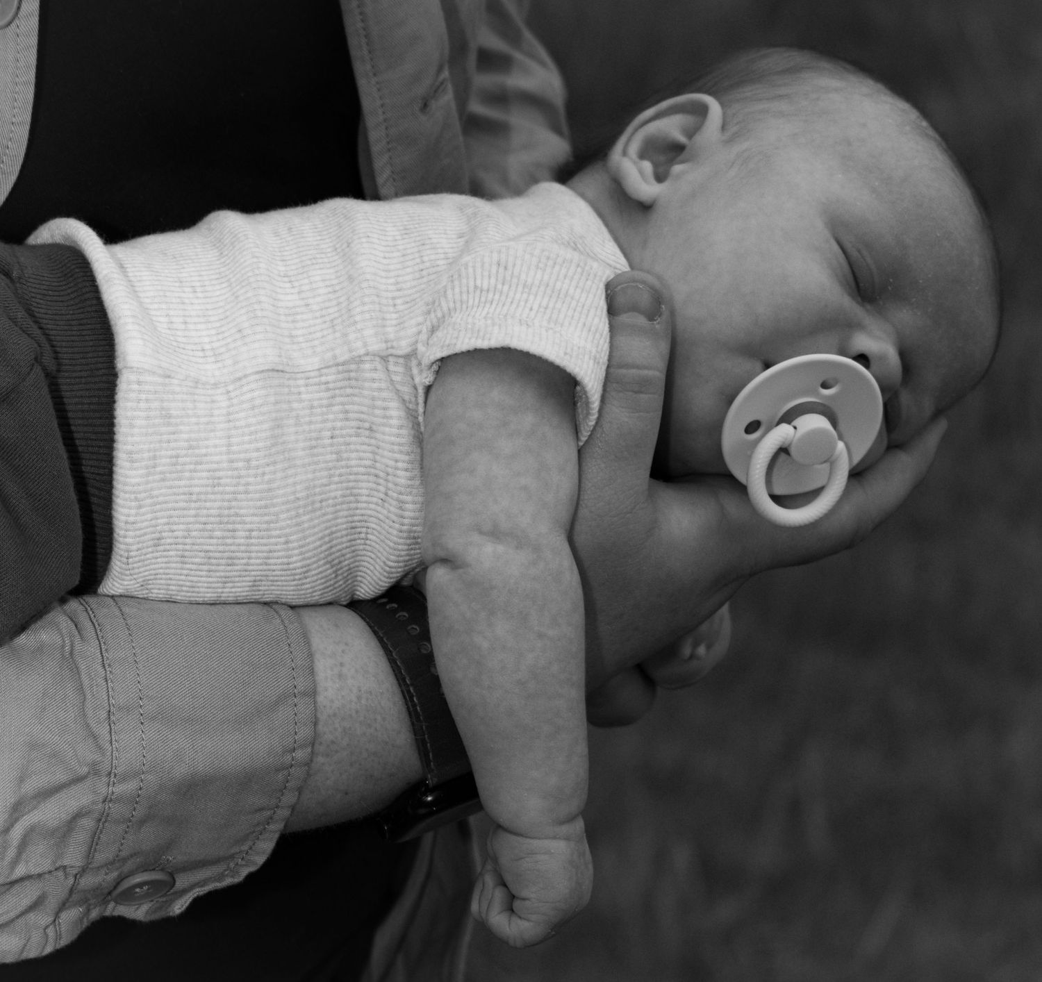 A black and white photo of a closeup on the dad holding his sleeping newborn baby on his arm