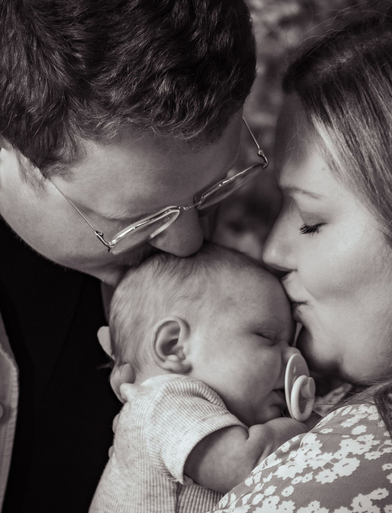 A black and white photo of a mom and dad holding and kissing their newborn baby's head