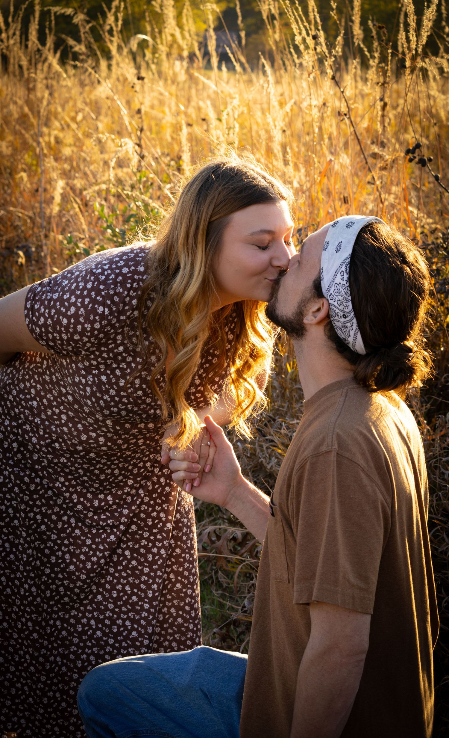 A happily engaged couple's photo in a field, kissing each other