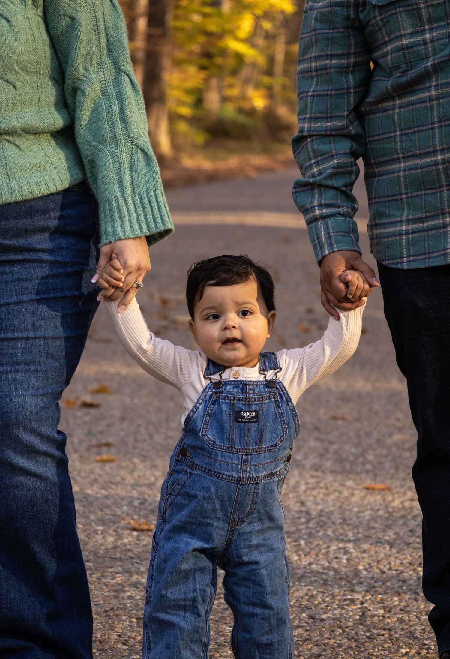 A mom and a dad holding each of their little boy's hands while walking down a gravel road