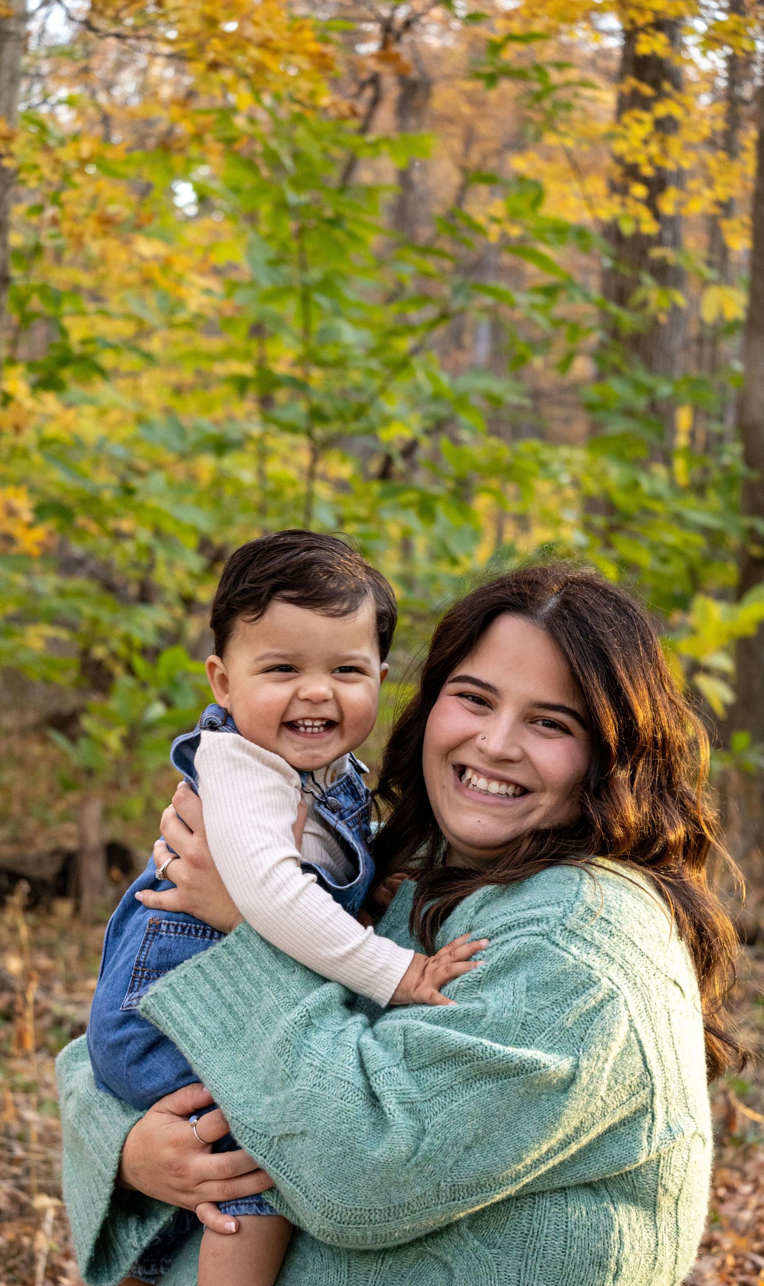 A mom in the woods holding her son and smiling