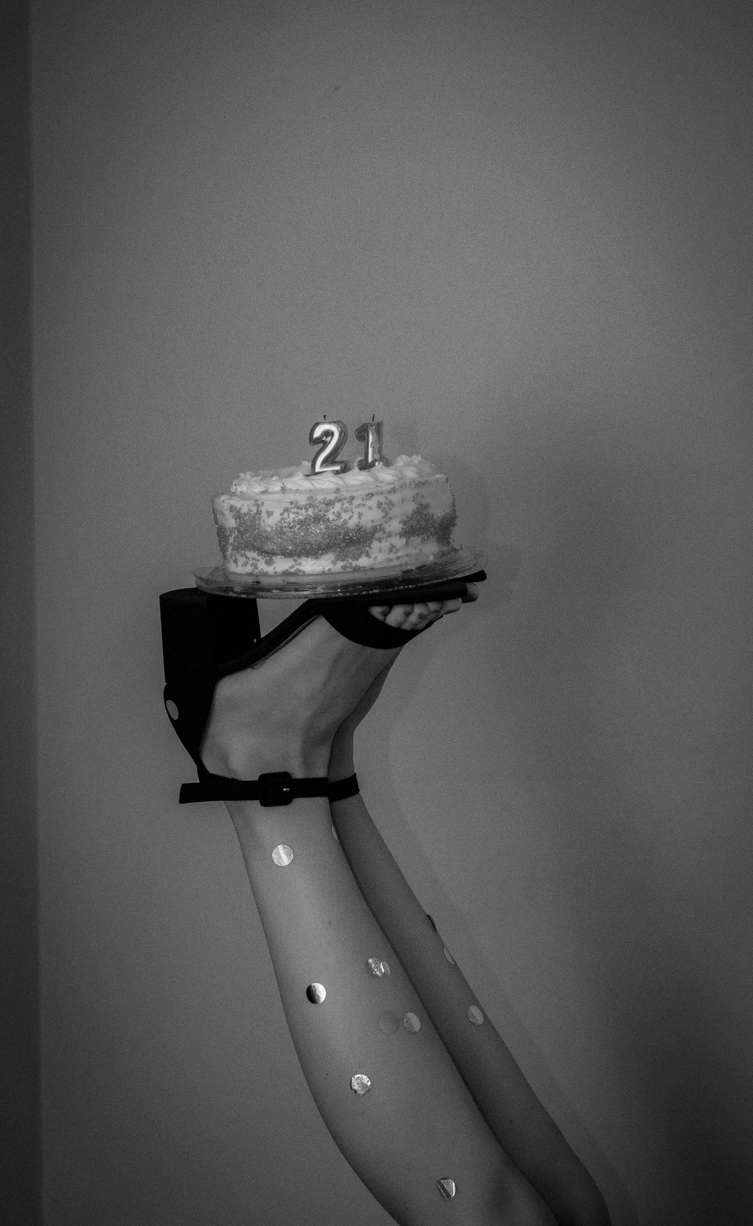 Woman celebrating her twenty-first birthday by holding up her birthday cake on her shoes, and with confetti on her legs