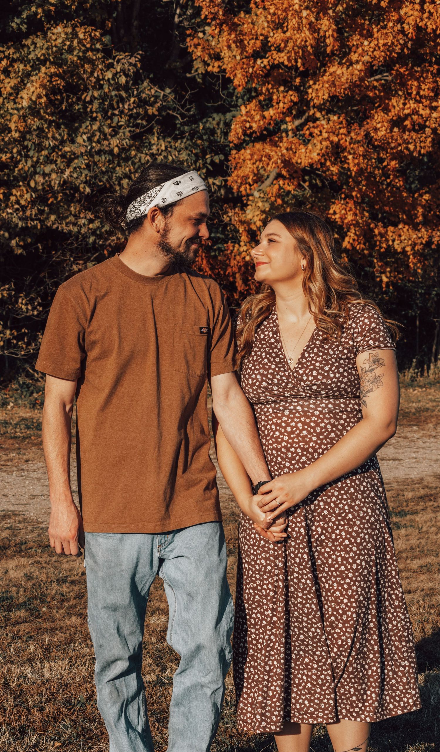 A happily engaged couple walking together and holding each other's hand, surrounded by colorful trees