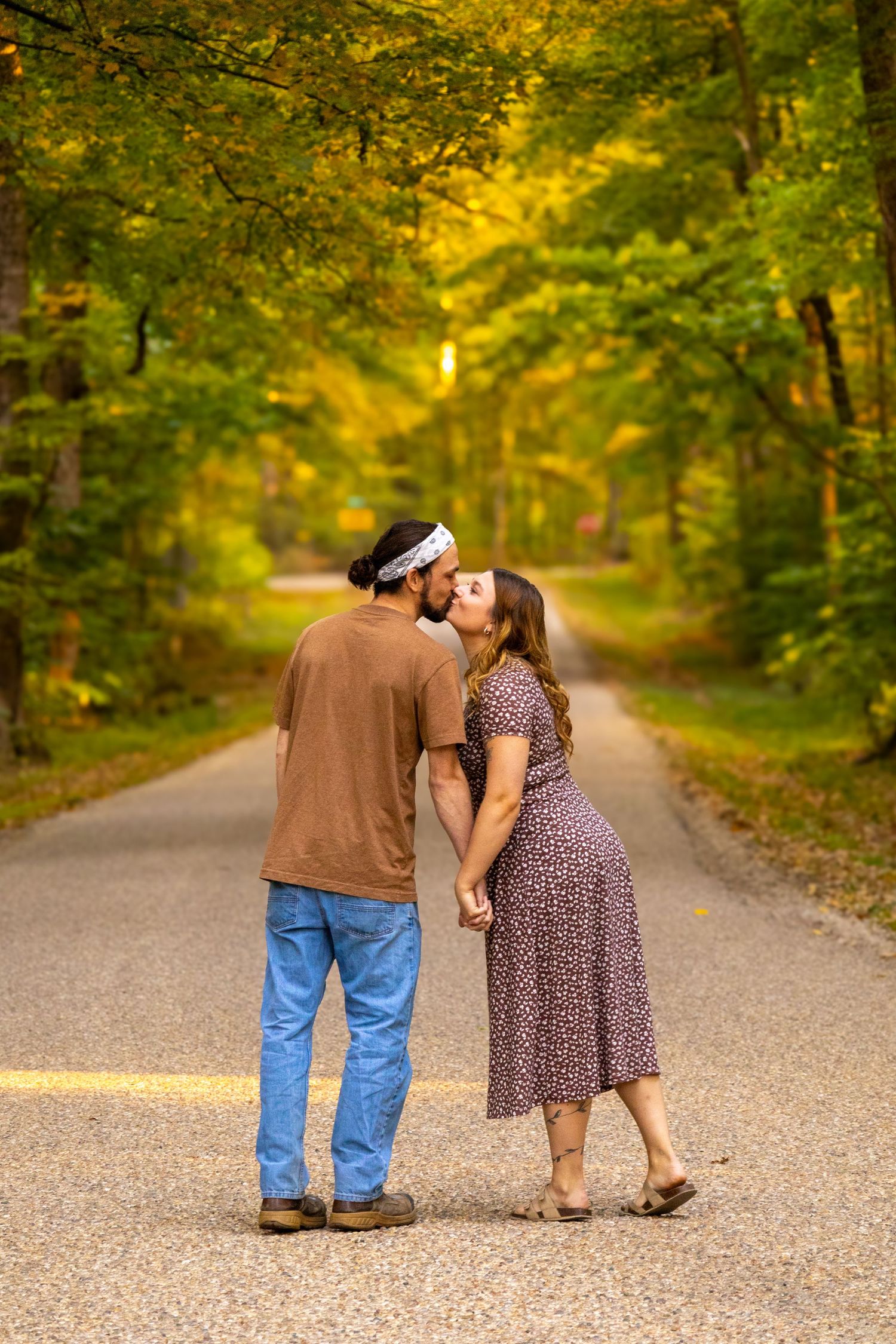 A young and happily engaged couple walking down a gravel road while kissing each other