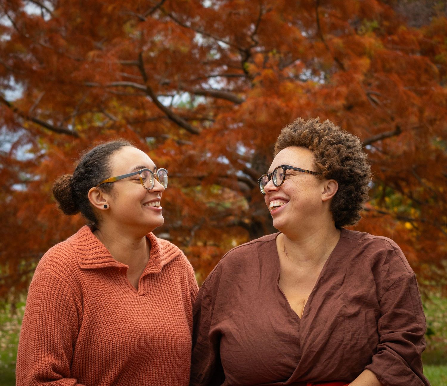 A photo of two women laughing and smiling at each other in the fall season
