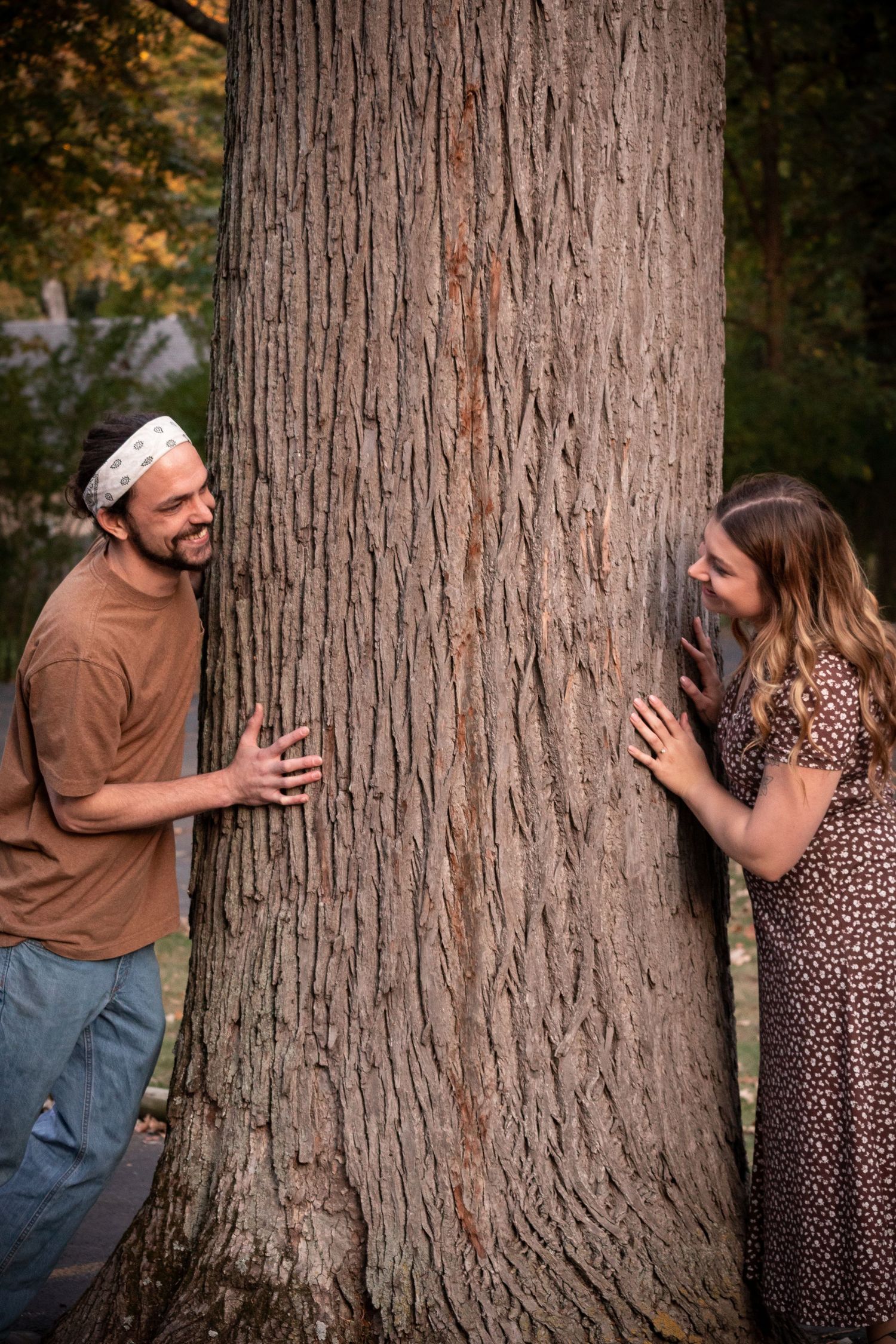 A happily engaged couple's photo playing hide and seek around a tree