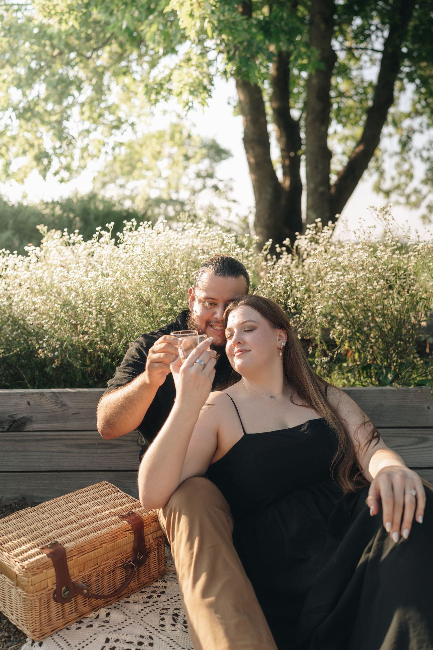Couple sitting together on a garden bench with a wicker picnic basket, sharing a romantic moment outdoors.