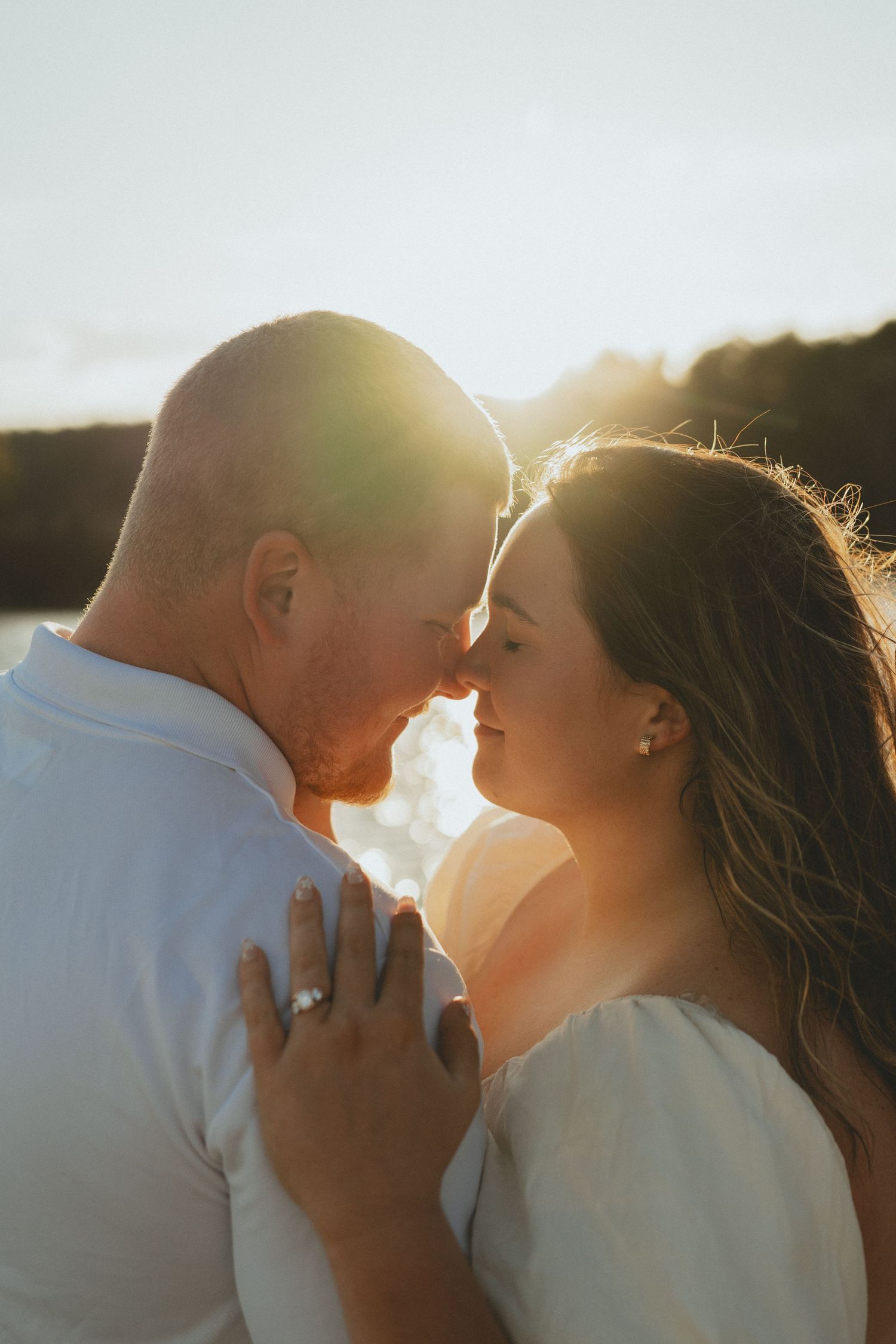 Couple sharing a romantic almost-kiss at golden hour sunset with warm backlight glowing behind them.