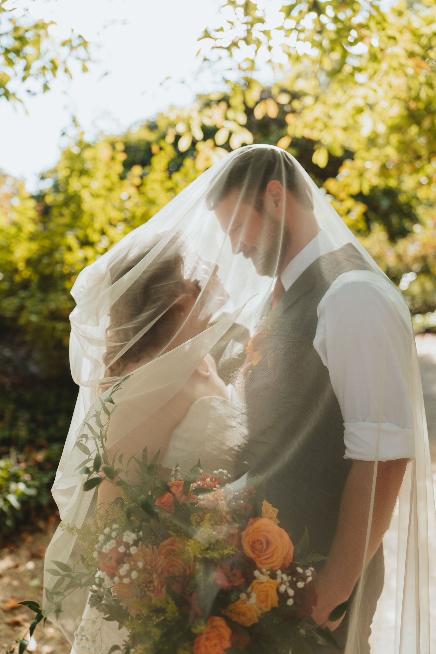 Bride and groom sharing a romantic moment under the brides veil with a colorful fall floral bouquet.