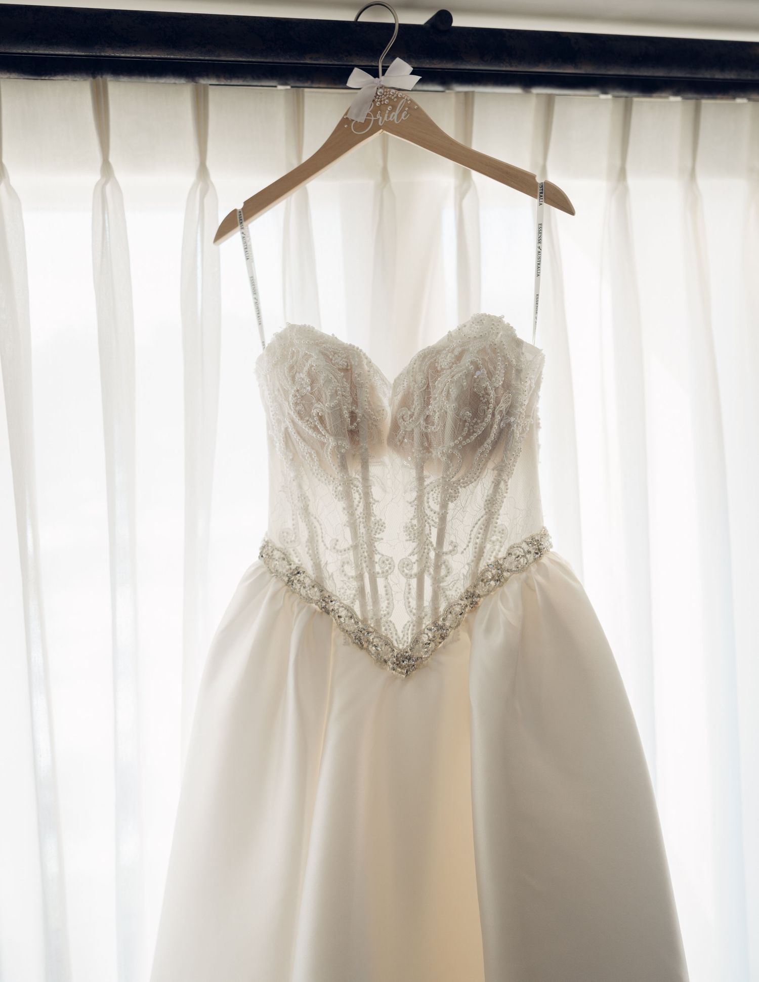 Beautiful strapless lace and satin wedding gown hanging on a personalized wooden hanger.
