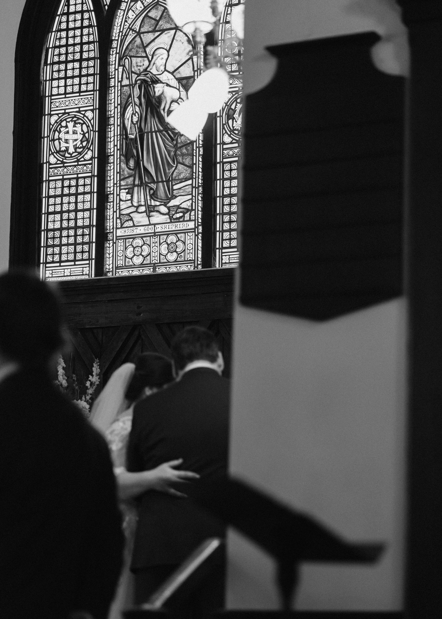 Black and white artistic shot of couple embracing before stunning stained glass window during church ceremony.