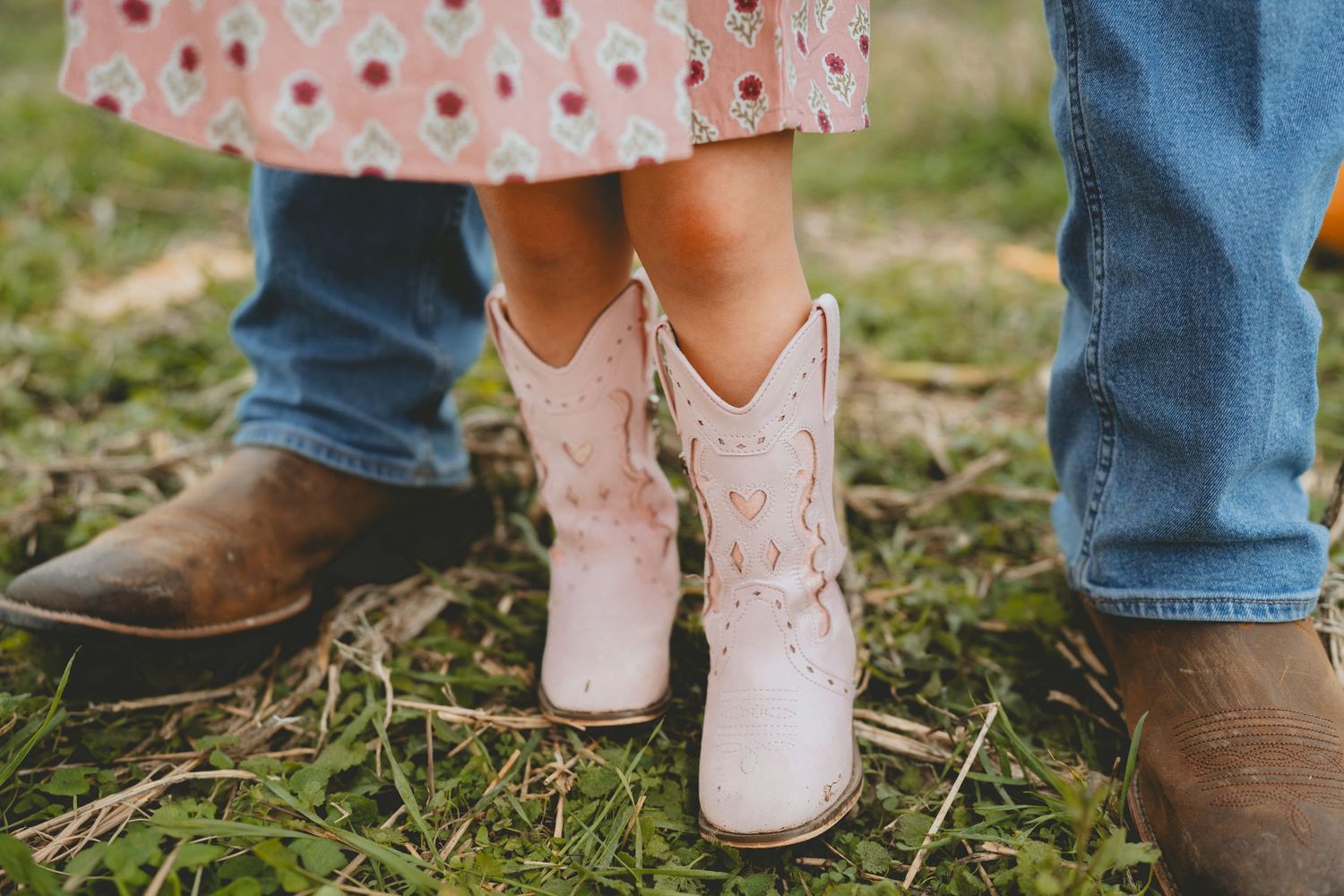 Close-up of child wearing pink cowboy boots standing between parents.