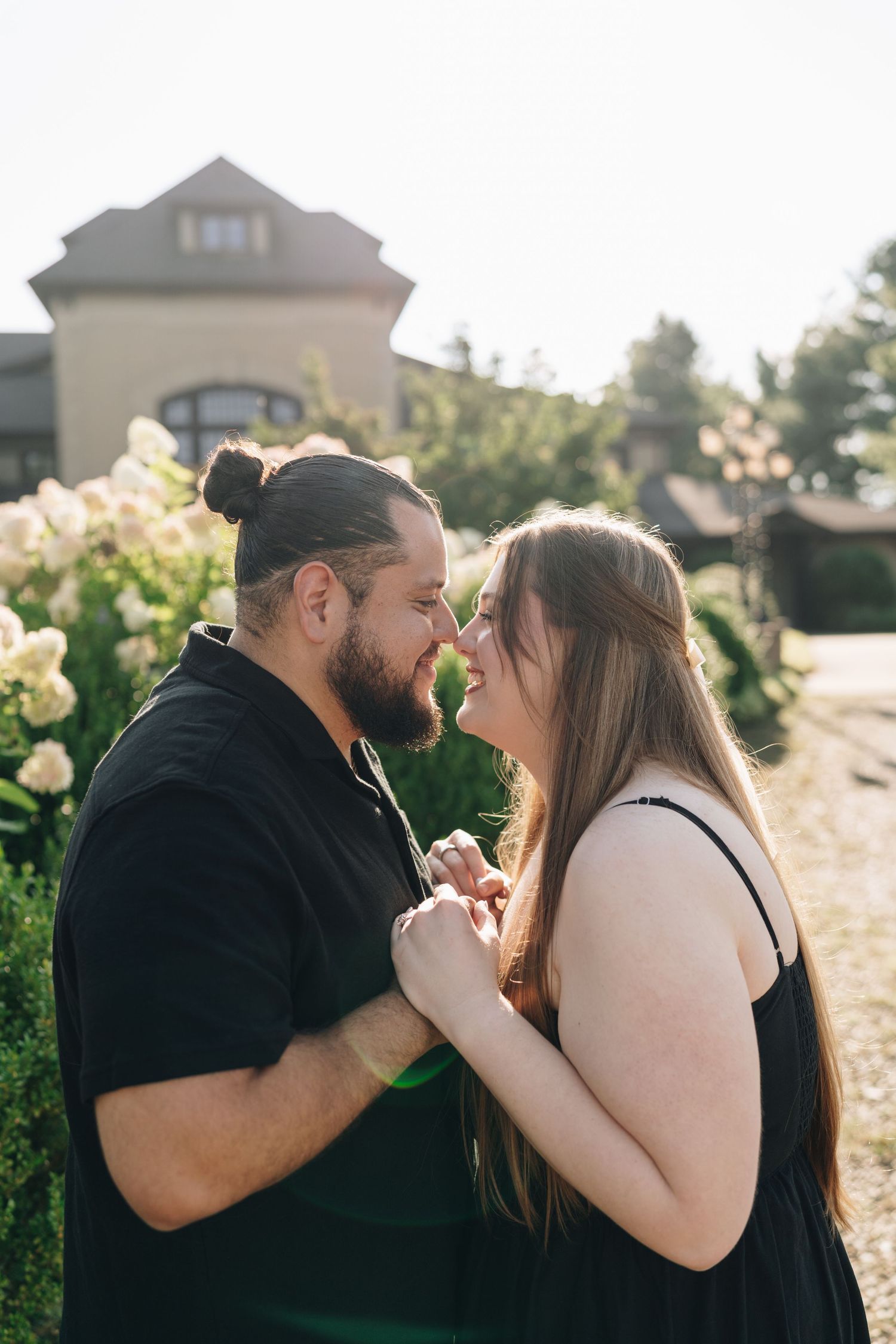 Romantic couple leaning in for a kiss while holding hands in front of blooming white flowers.