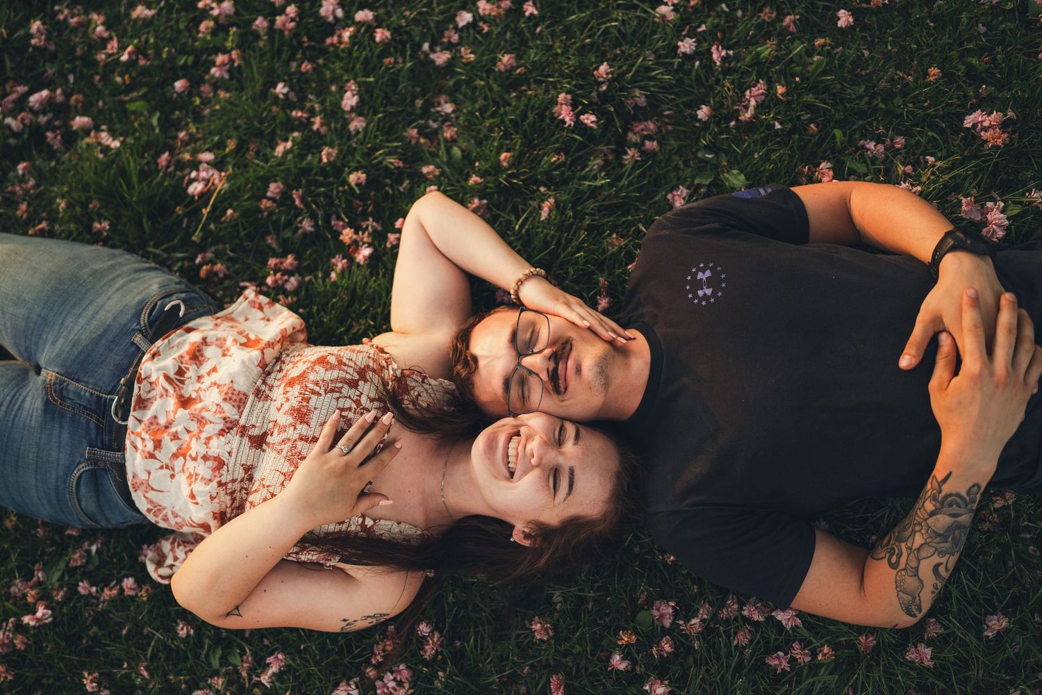 Happy couple lying on flower-covered grass smiling at each other in warm sunlight.