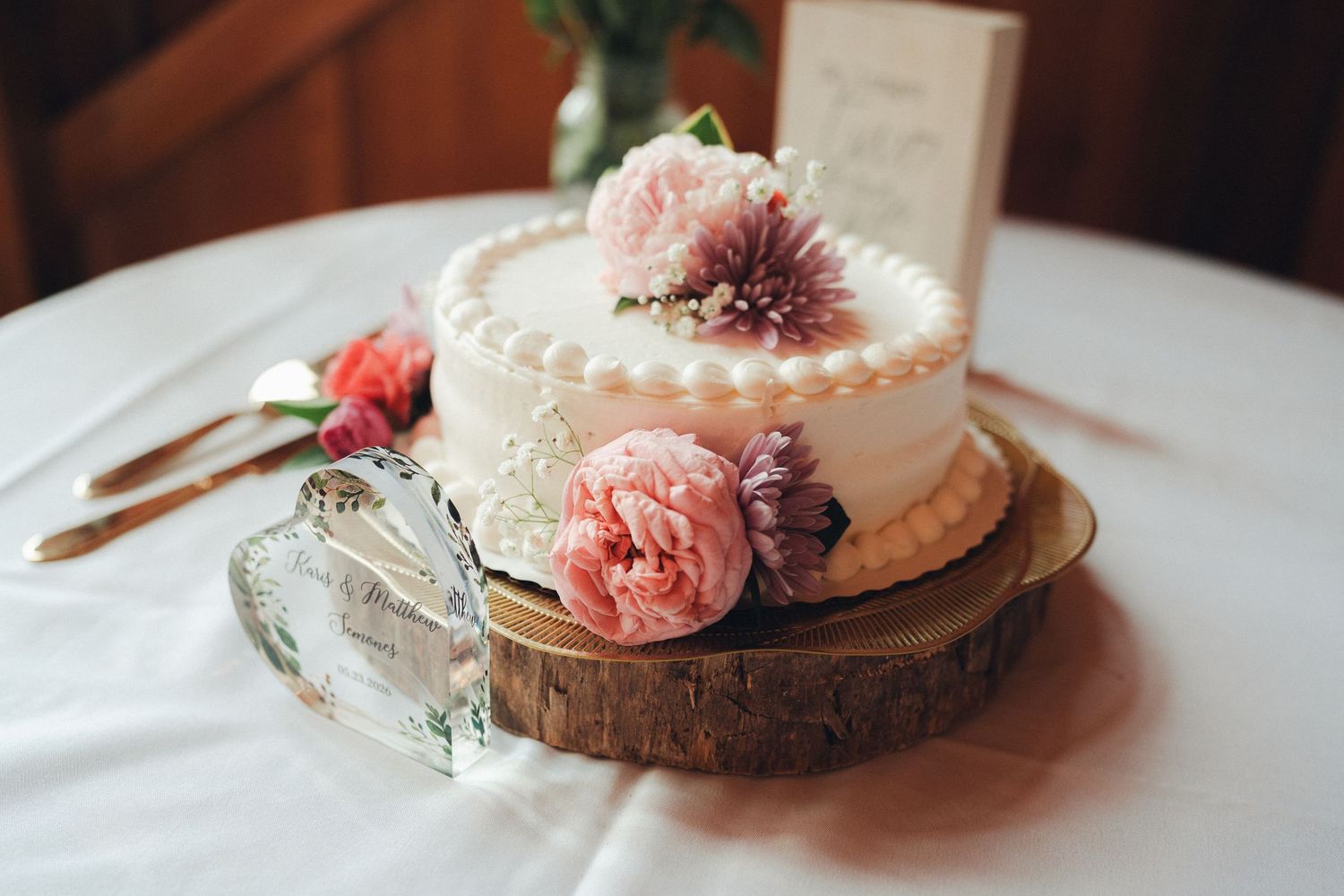 Elegant single-tier wedding cake decorated with fresh pink flowers and pearls on a rustic wood slice stand.