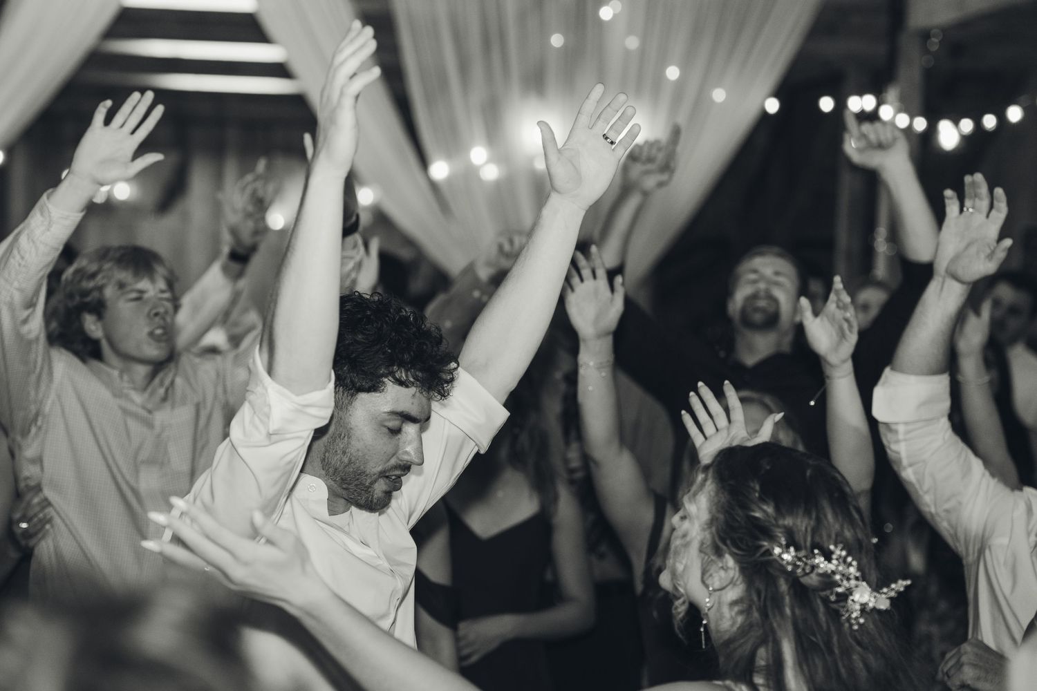 Joyful wedding guests dancing with hands raised at a lively black and white reception party.