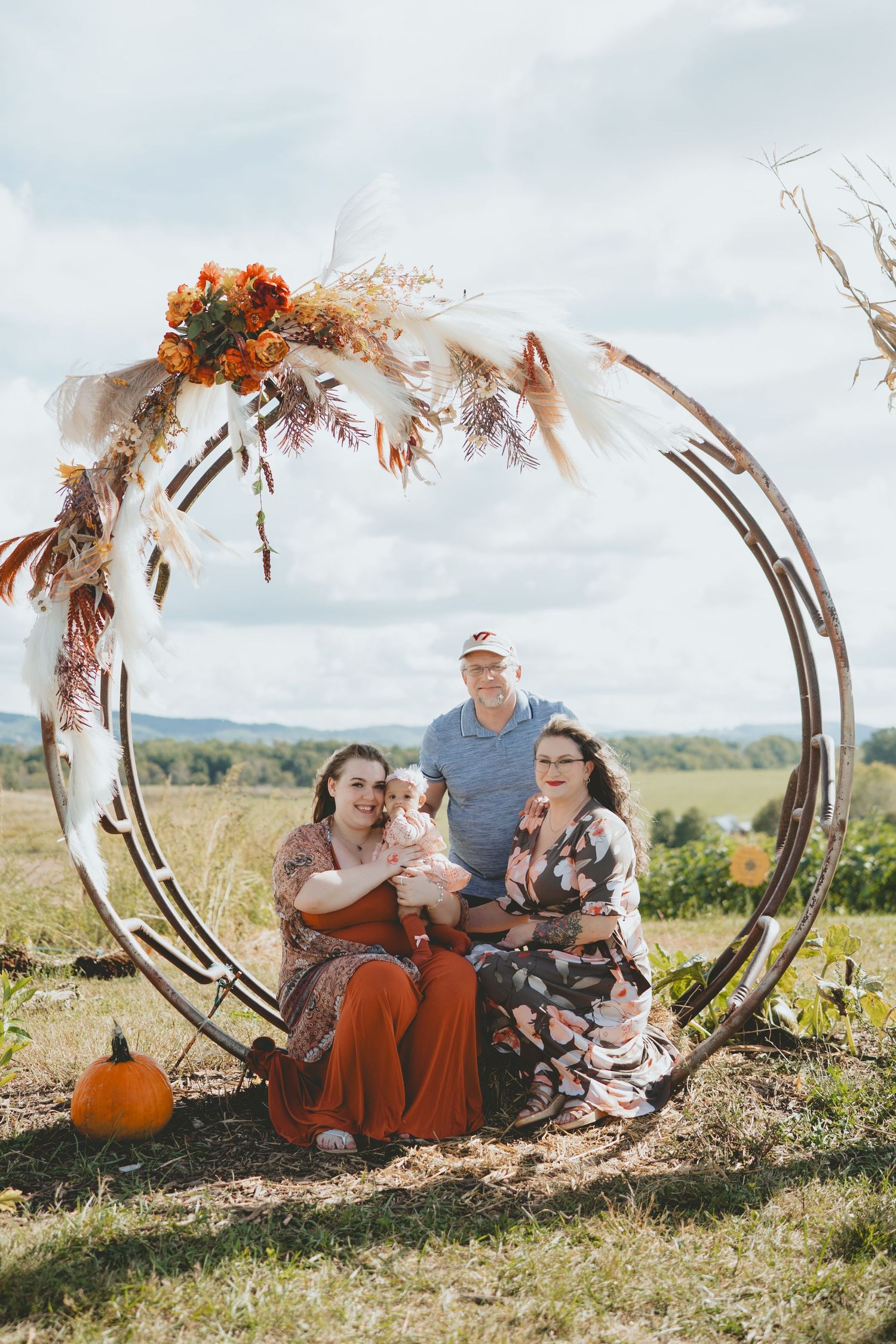 Happy family with baby posing inside a circular floral arch at an autumn farm setting.