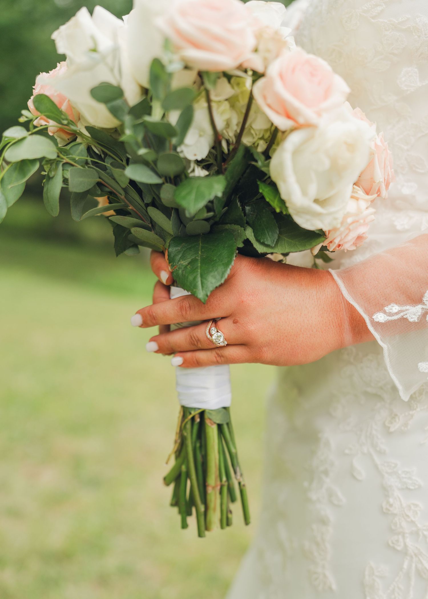 Close-up of bride holding elegant pink and white rose wedding bouquet with diamond engagement ring visible.