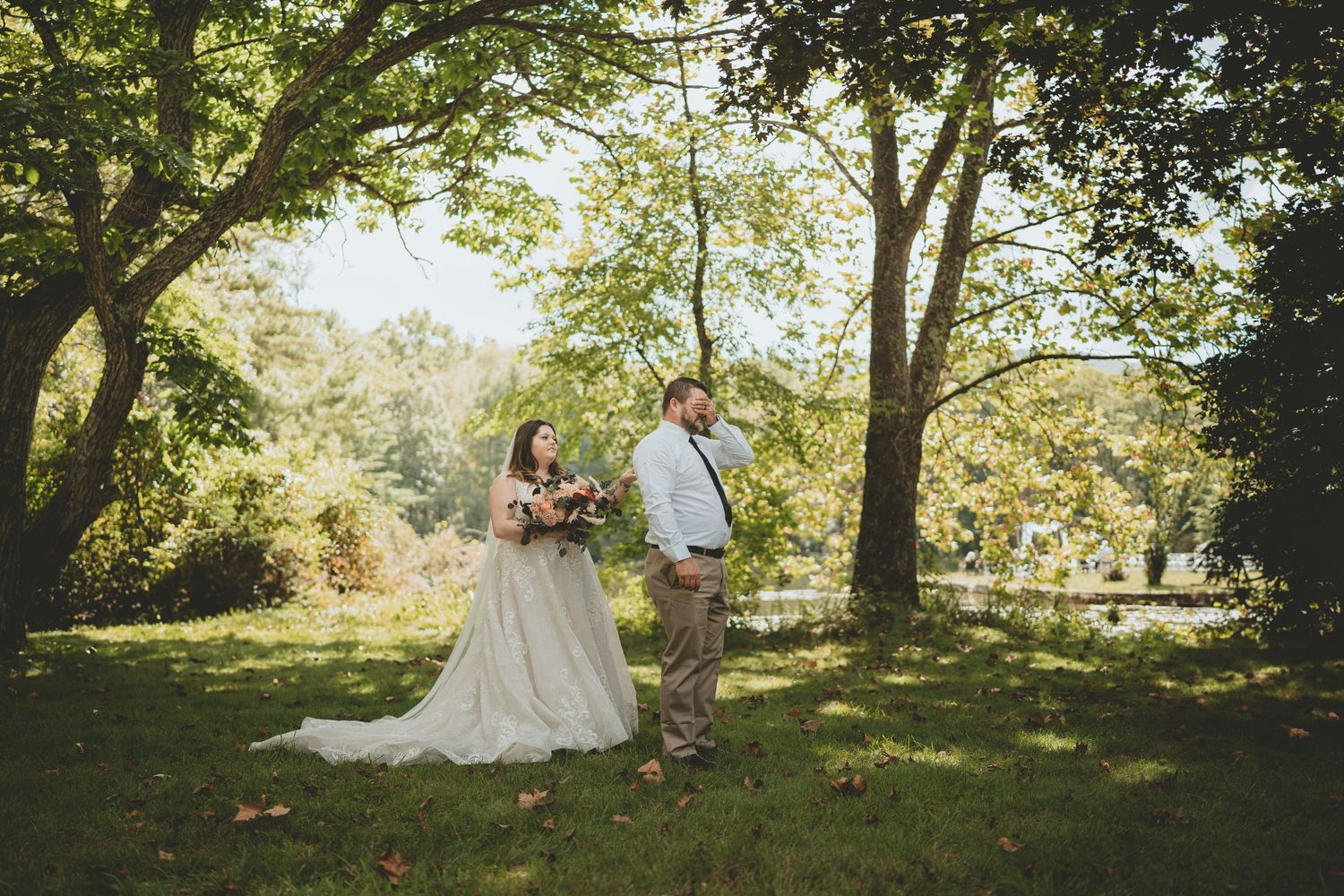 Bride in lace gown and groom in suspenders share a romantic moment in a sunlit garden setting.