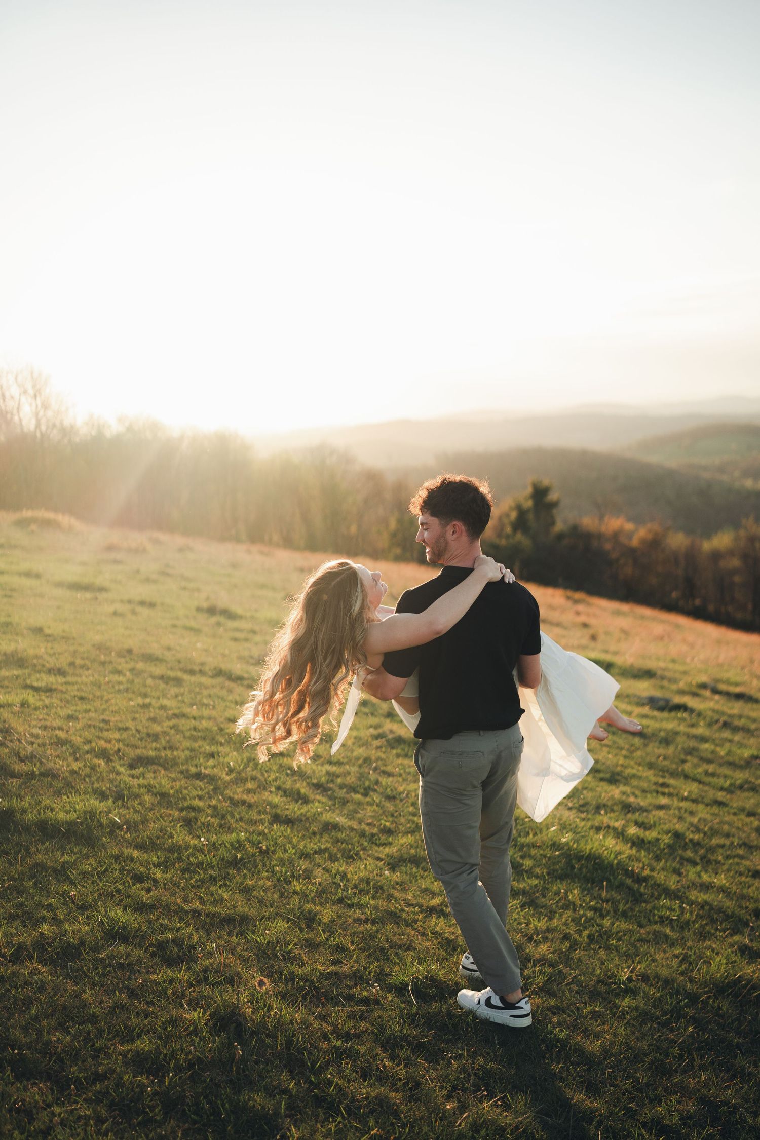 Couple dancing and spinning on a green hillside with stunning golden sunset backdrop.
