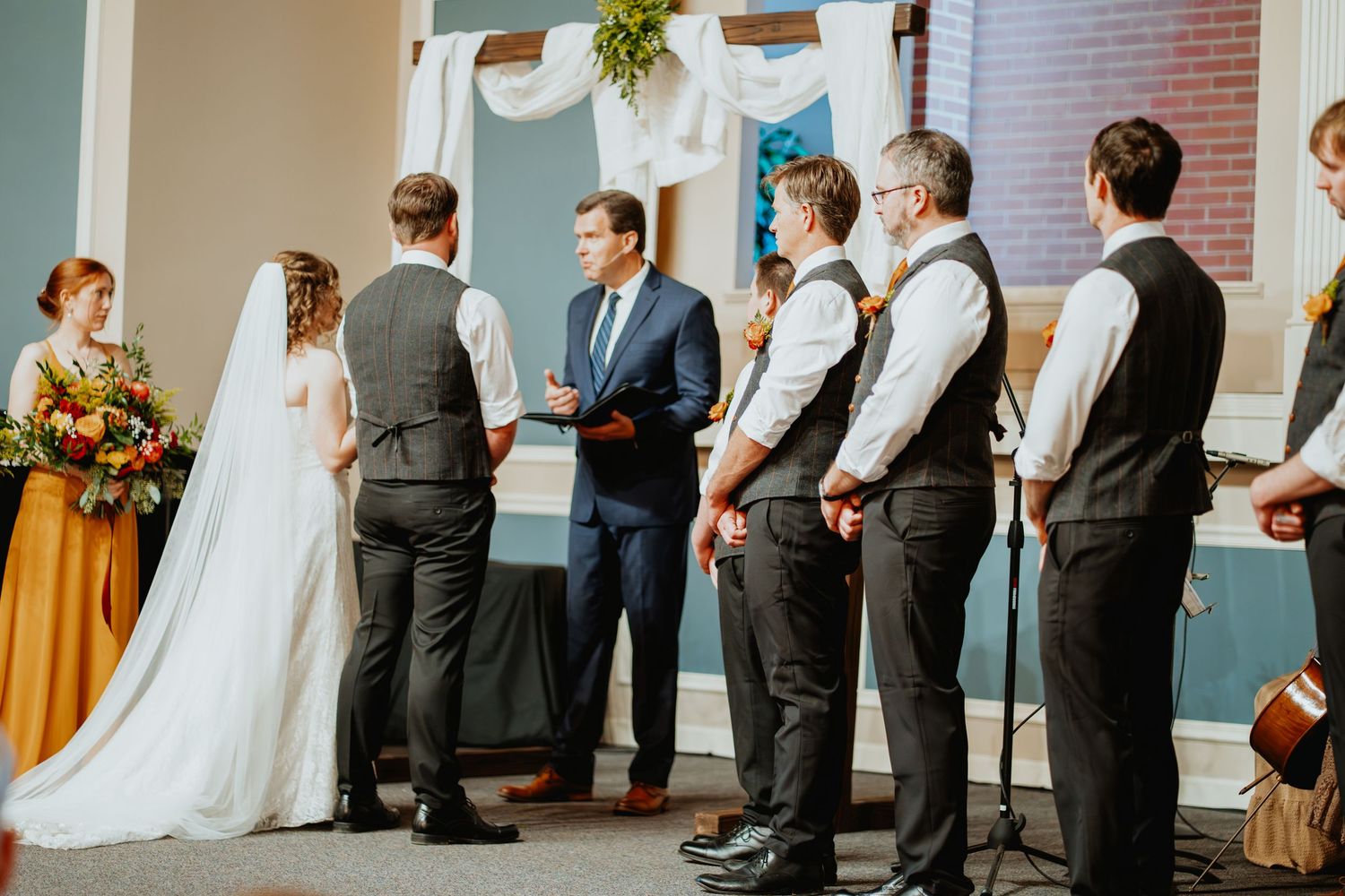 Wedding ceremony with bride, groom, officiant, and groomsmen at a decorated church altar.