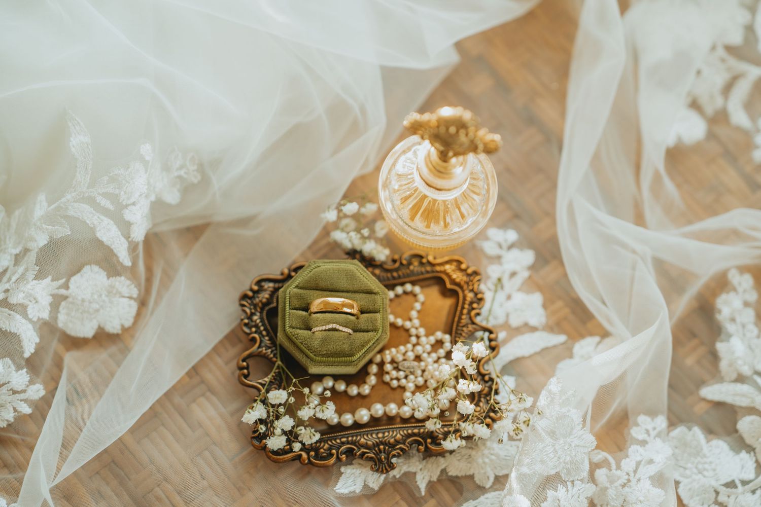 Wedding rings on ornate gold tray with pearls, perfume bottle, and lace veil.
