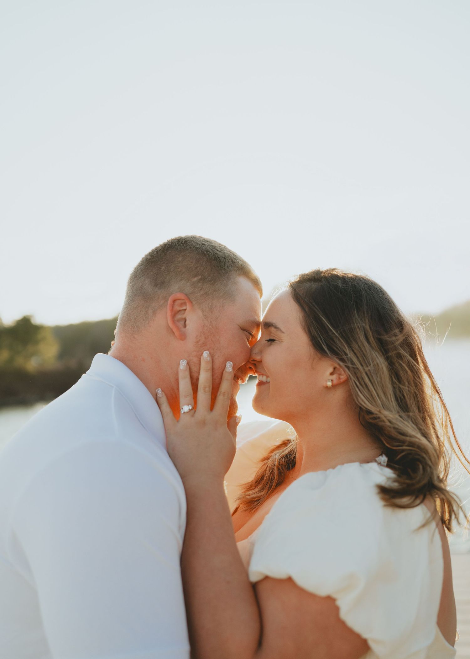 Engaged couple touching foreheads and smiling with engagement ring visible during a romantic sunset beach session.