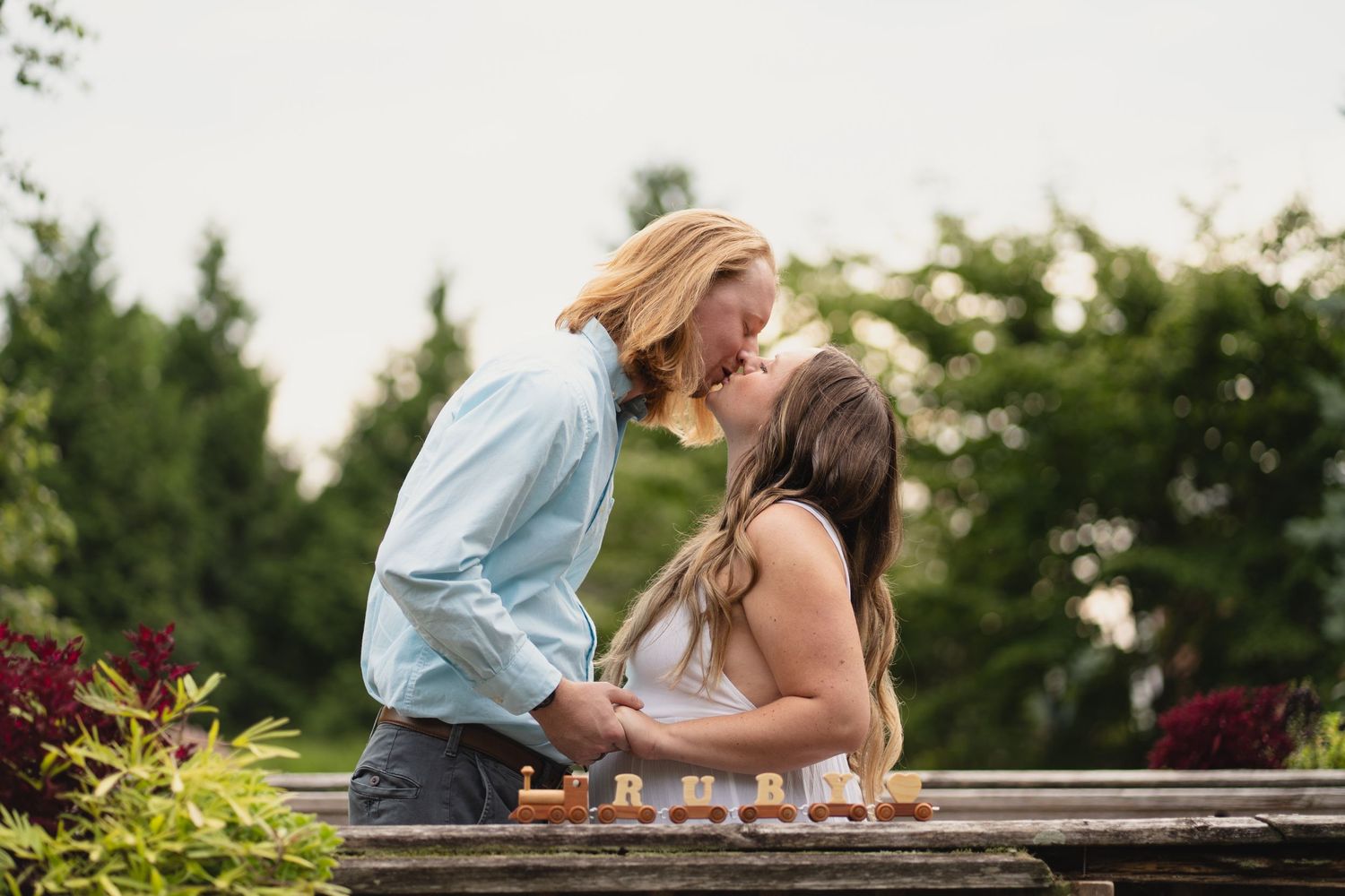 Couple sharing a tender kiss over a chess board surrounded by lush green garden foliage.