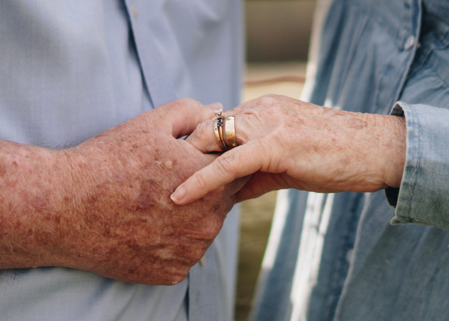 Close-up of elderly couple holding hands showing gold wedding rings as symbol of lasting love.