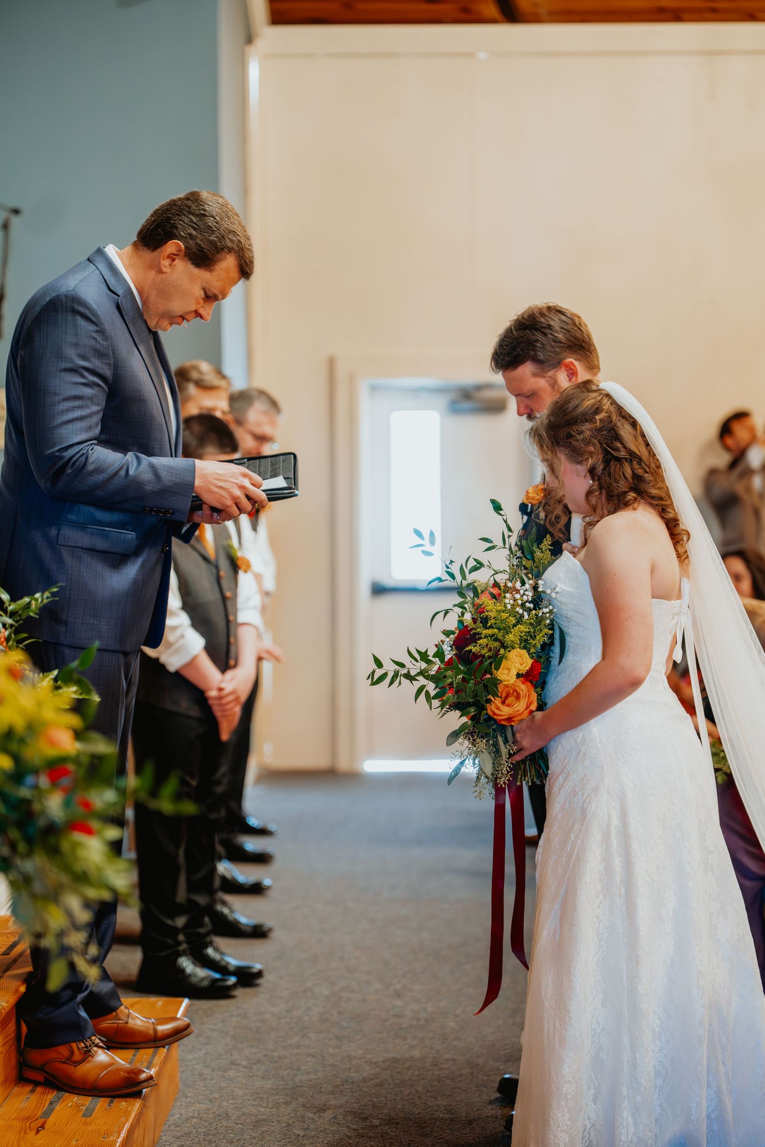 Officiant presents rings to the bowing bride and groom during an indoor wedding ceremony.