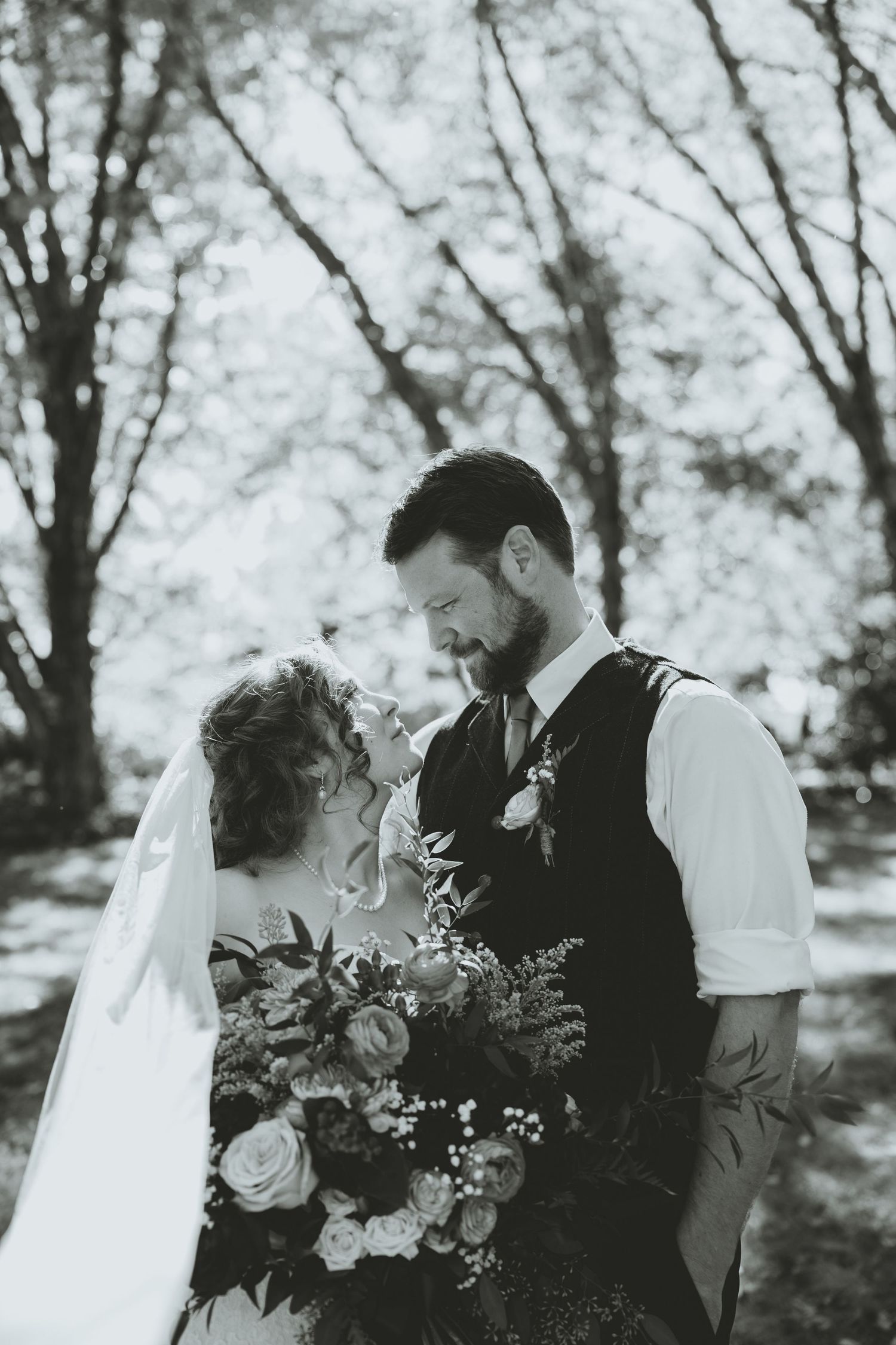 Black and white photo of bride and groom sharing a romantic moment with a lush bridal bouquet.