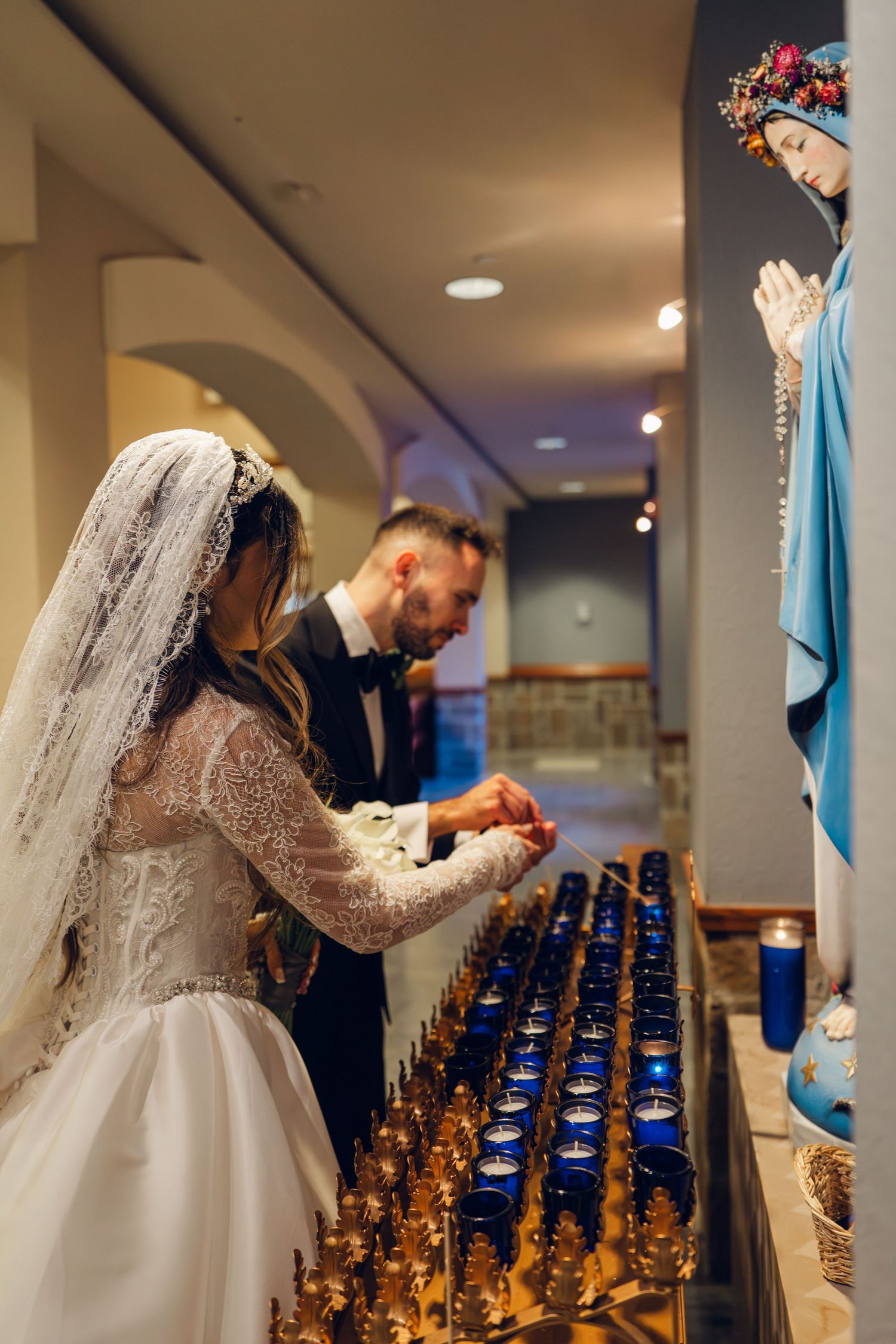 Bride and groom light candles together before Virgin Mary statue during Catholic wedding ceremony.