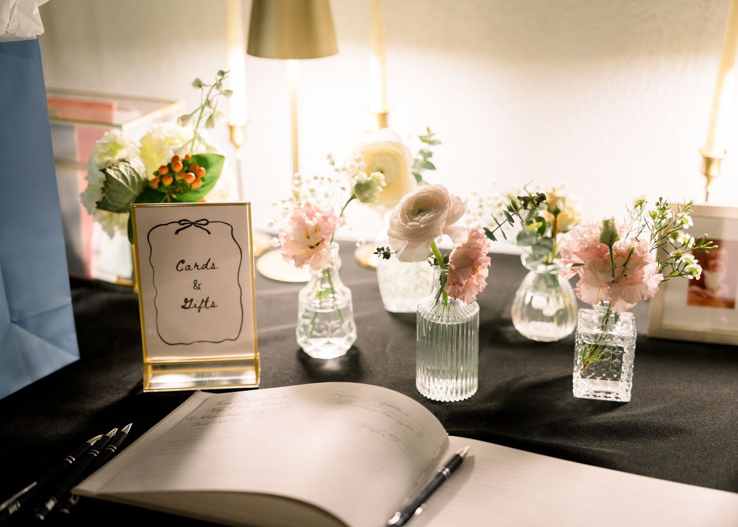 Wedding cards and gifts table decorated with small bud vases of pink and white flowers and open guest book.
