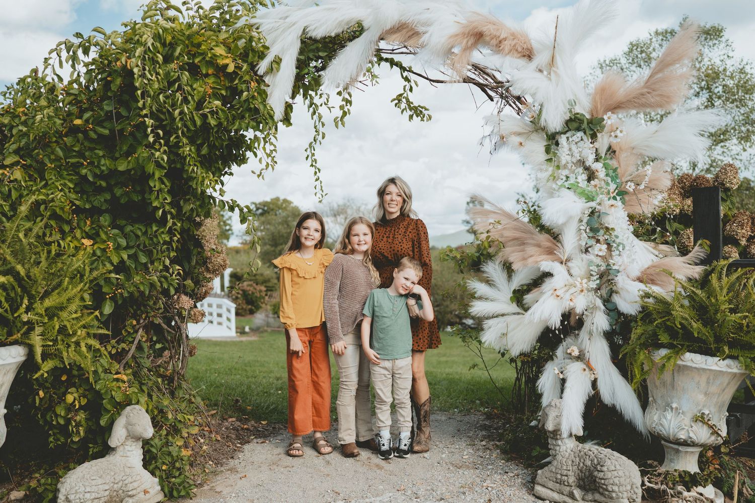 Woman and three children posing under a floral garden arch with stone statues.