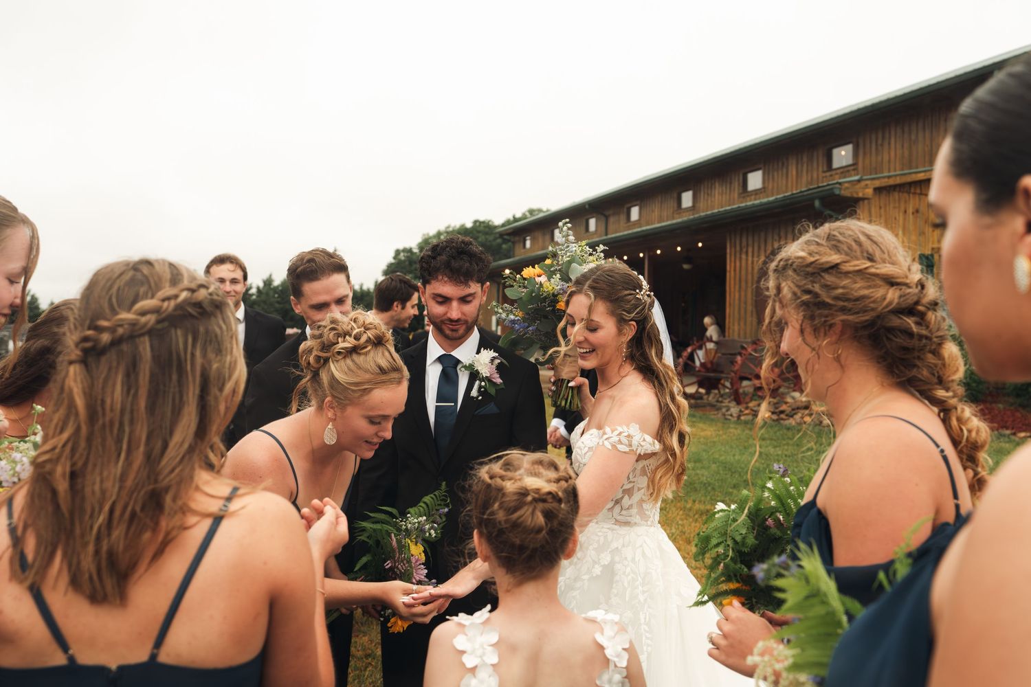 Bride and groom surrounded by bridesmaids in navy dresses celebrating after outdoor barn wedding ceremony.