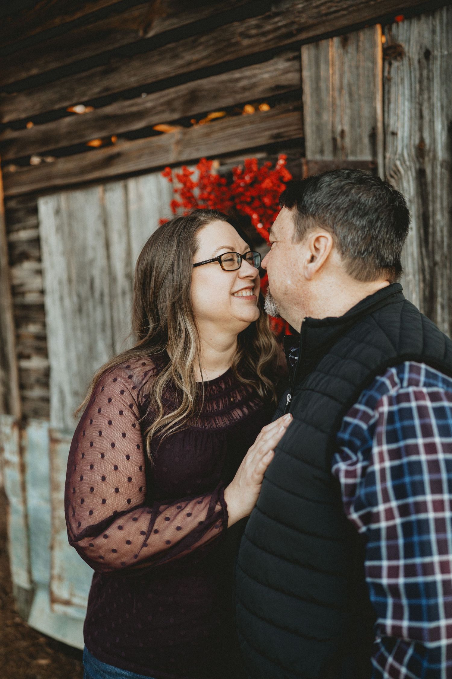 Couple sharing a tender kiss near a rustic wooden barn wall.