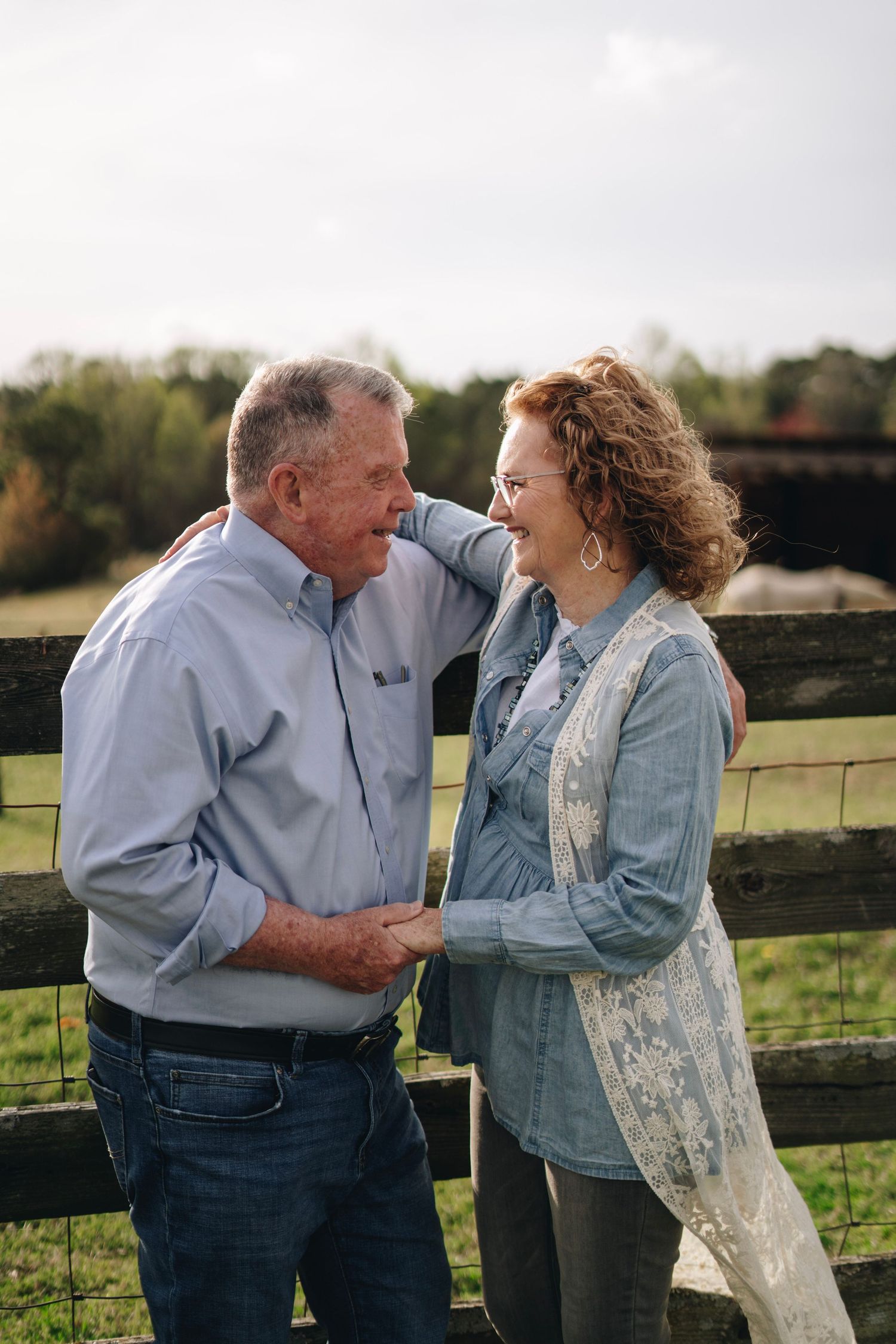 Happy older couple holding hands and smiling at each other by rustic wooden farm fence.
