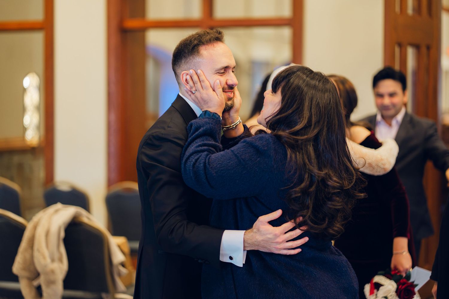 Emotional groom receives congratulatory kiss from family member at wedding celebration.