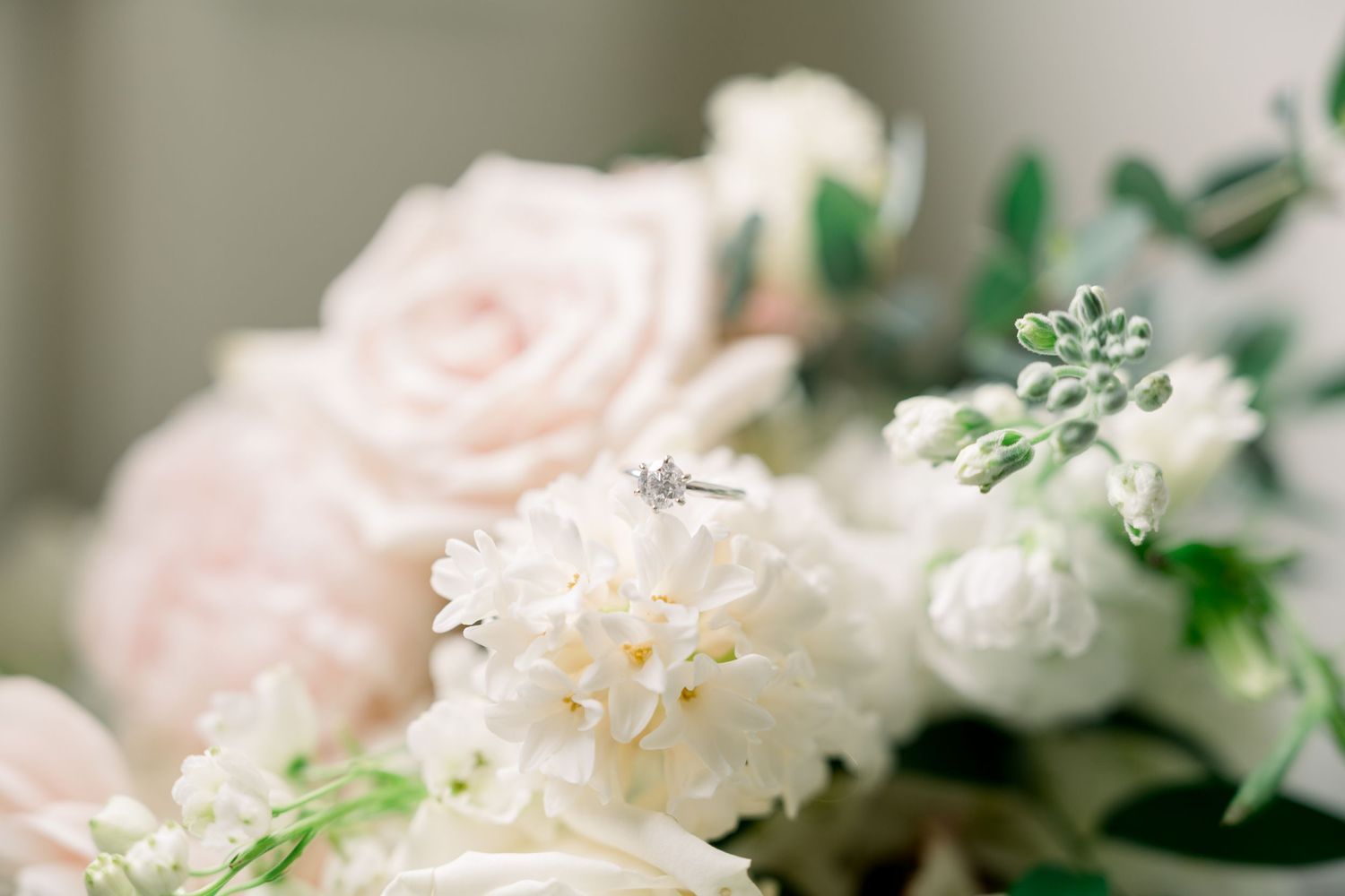 Diamond engagement ring resting on white and blush pink floral wedding bouquet.