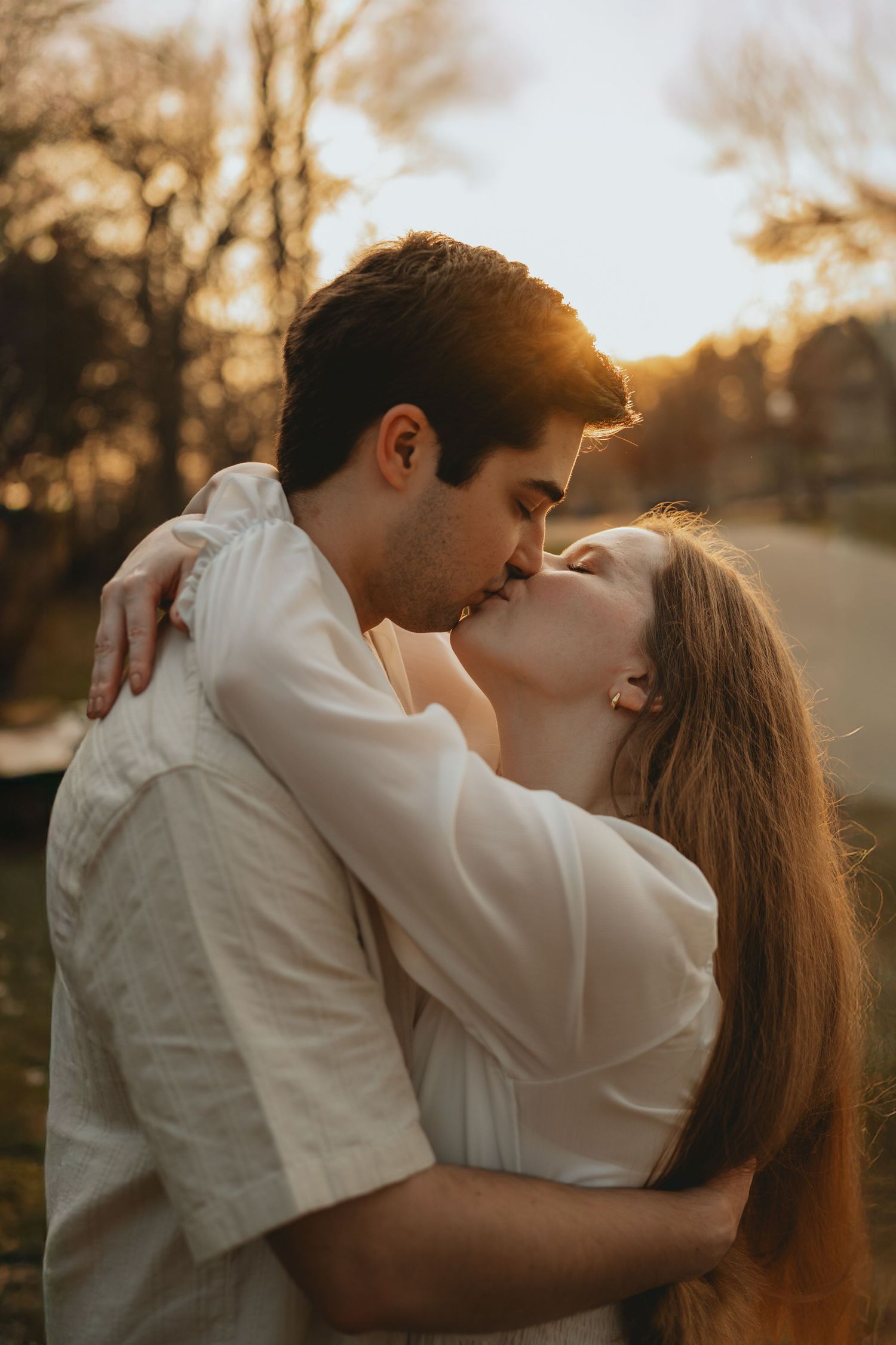 Couple sharing a romantic kiss at golden hour sunset in a park, embracing tenderly.