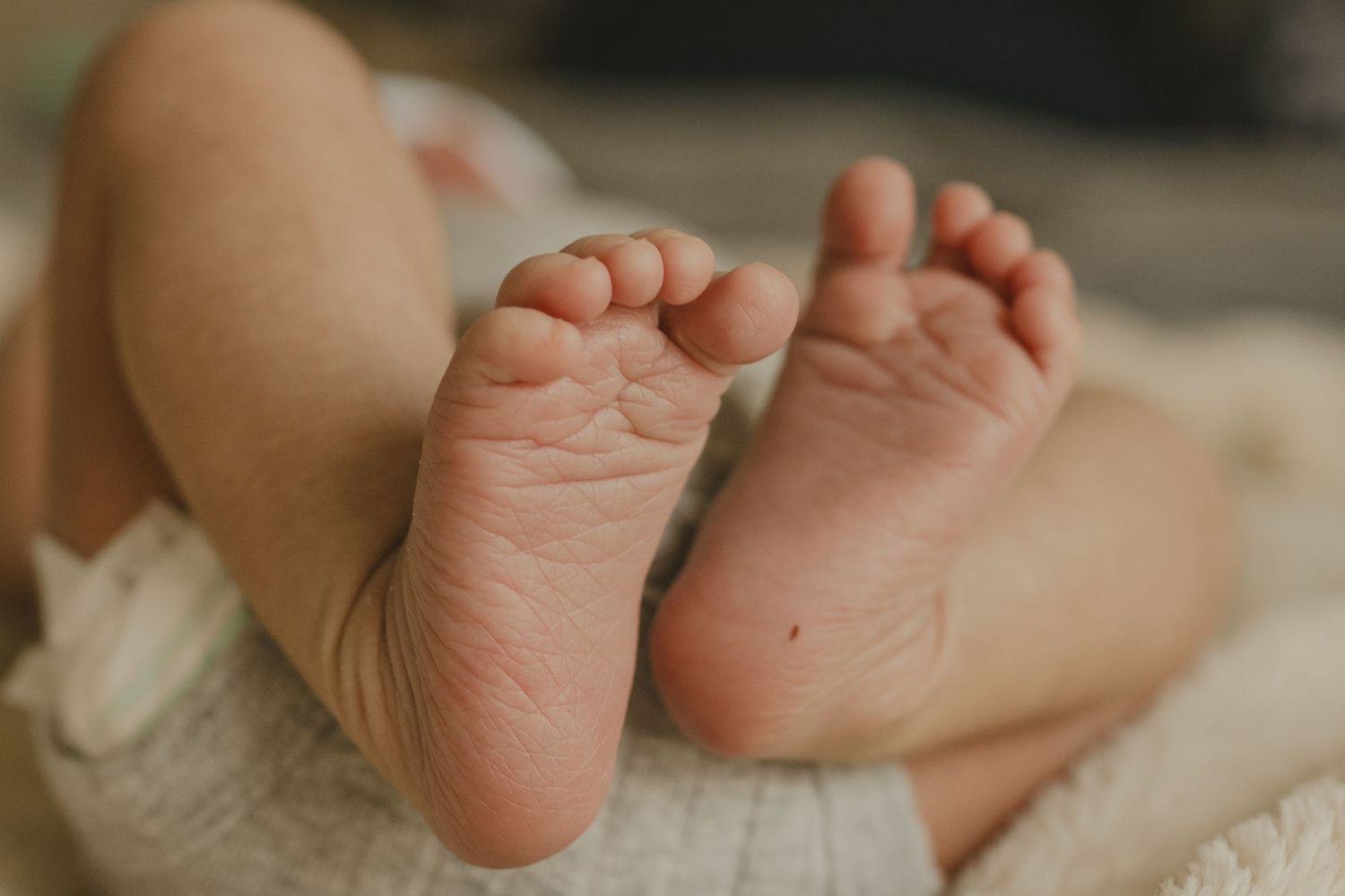 Close-up of soft, wrinkled newborn baby feet resting on a white blanket.