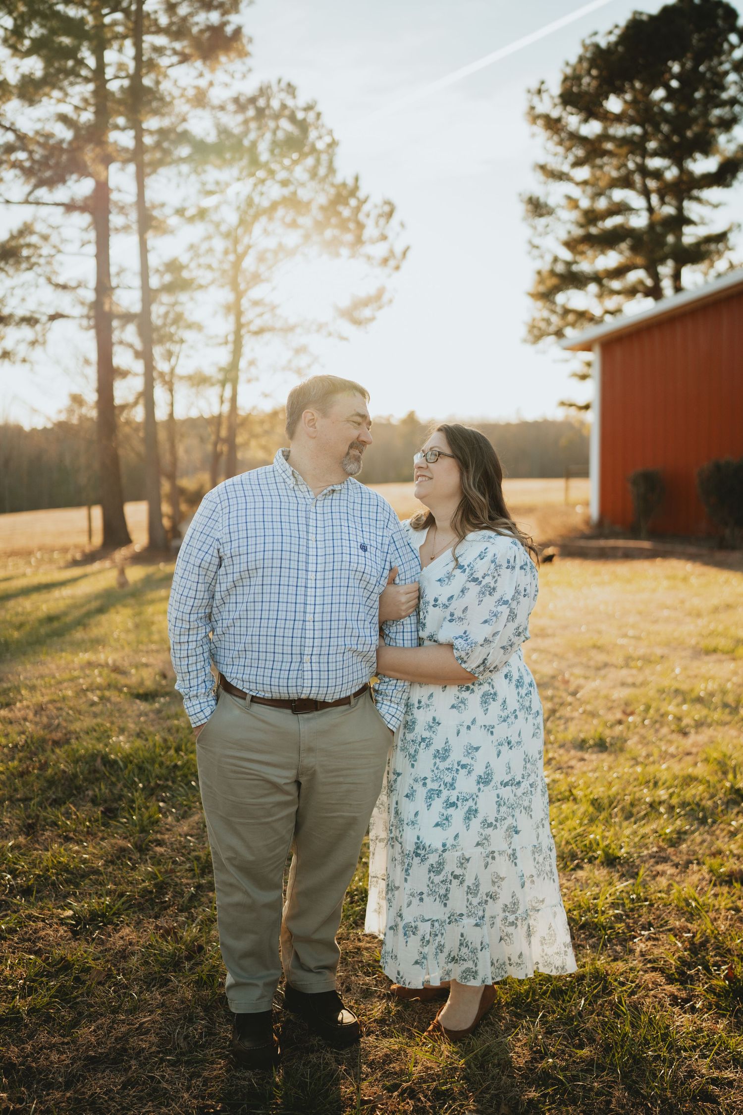 Happy couple embracing and laughing together at sunset near a red barn on a farm property.