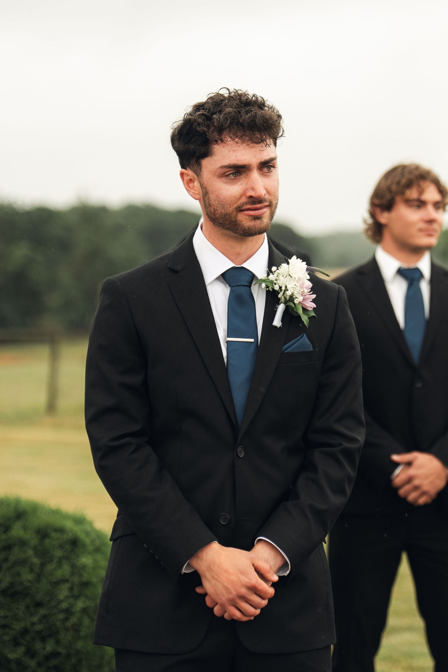 Handsome groom in black suit with floral boutonniere standing at the altar awaiting his bride outdoors.