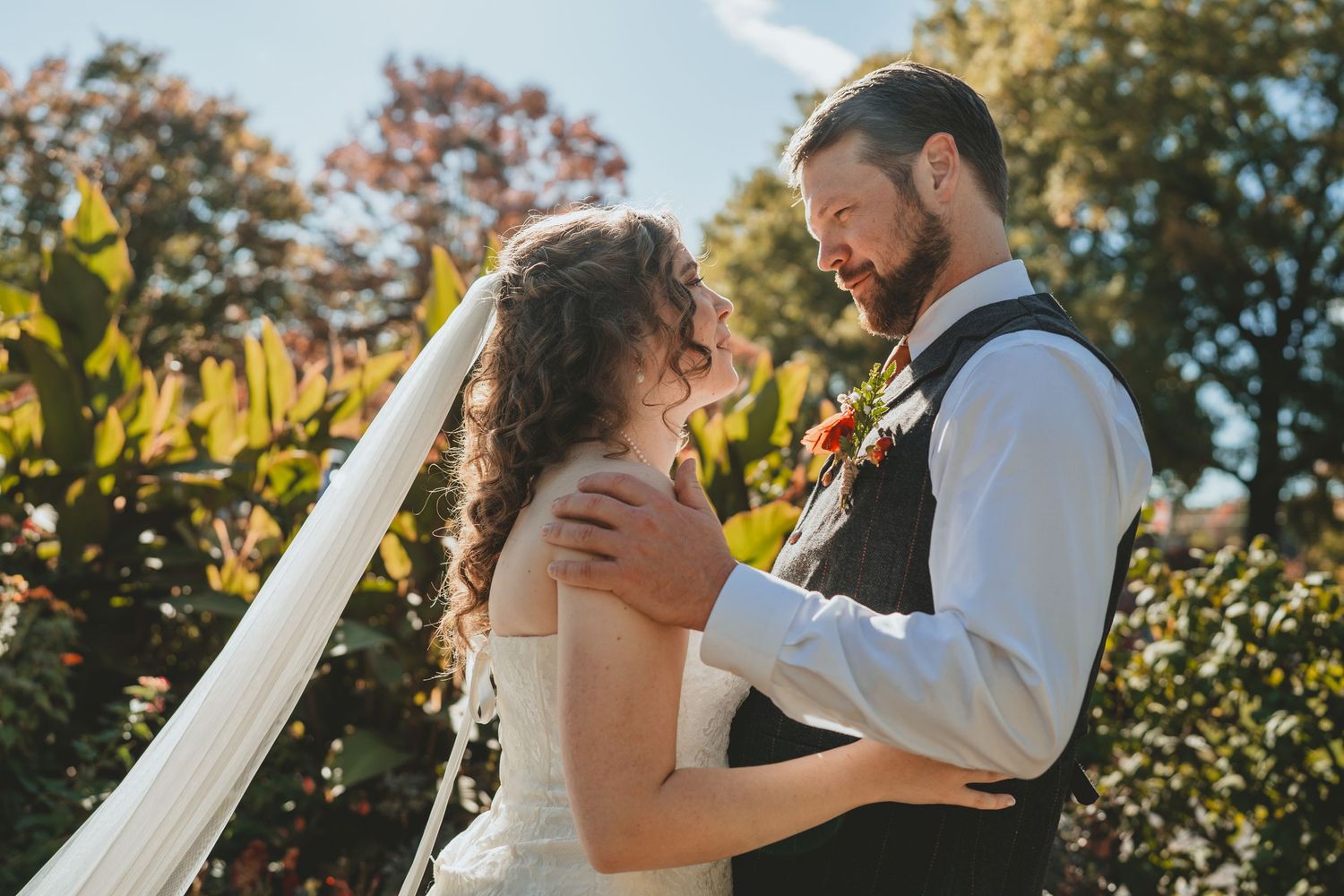 Bride and groom sharing tender moment embracing outdoors surrounded by fall foliage.
