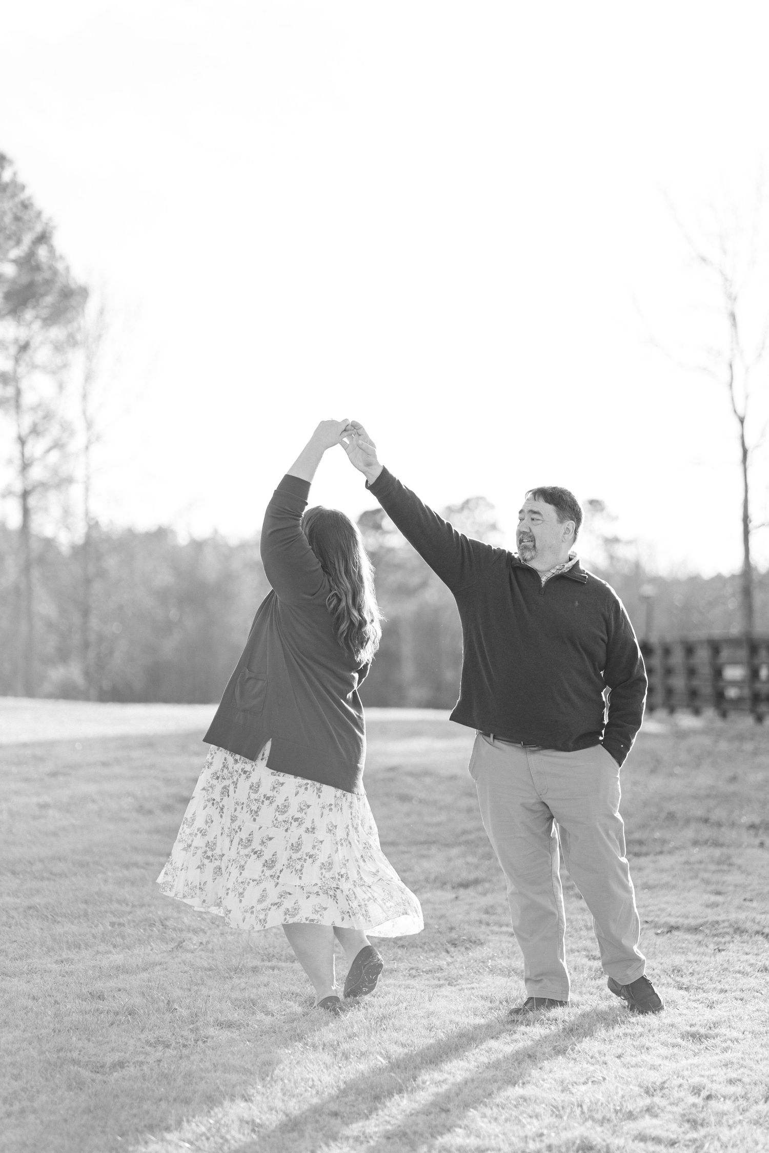 Black and white photo of a man twirling a woman in a floral skirt in an open field.