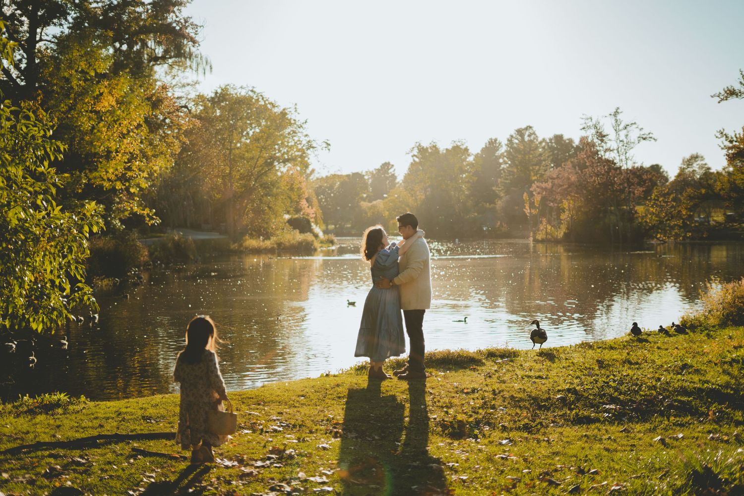 Family of four enjoying sunny autumn day by a peaceful duck pond surrounded by fall foliage.