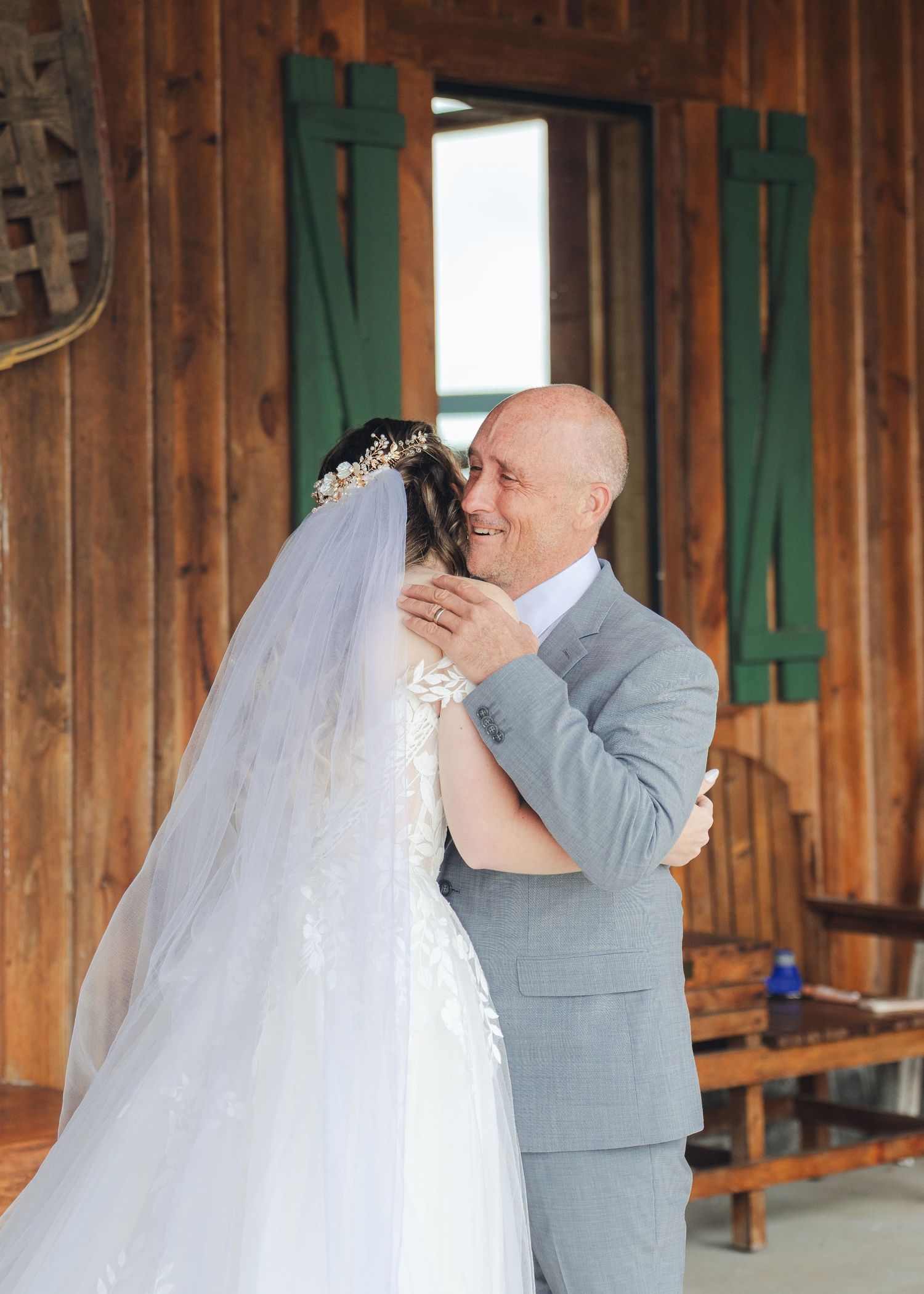 Father embracing his daughter the bride in a heartfelt first look moment inside a rustic wooden barn.
