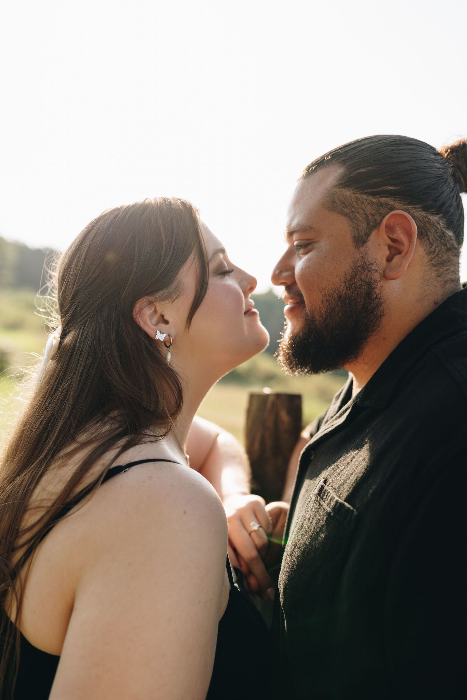 Romantic couple about to kiss in golden backlit sunlight with rustic wooden fence in background.